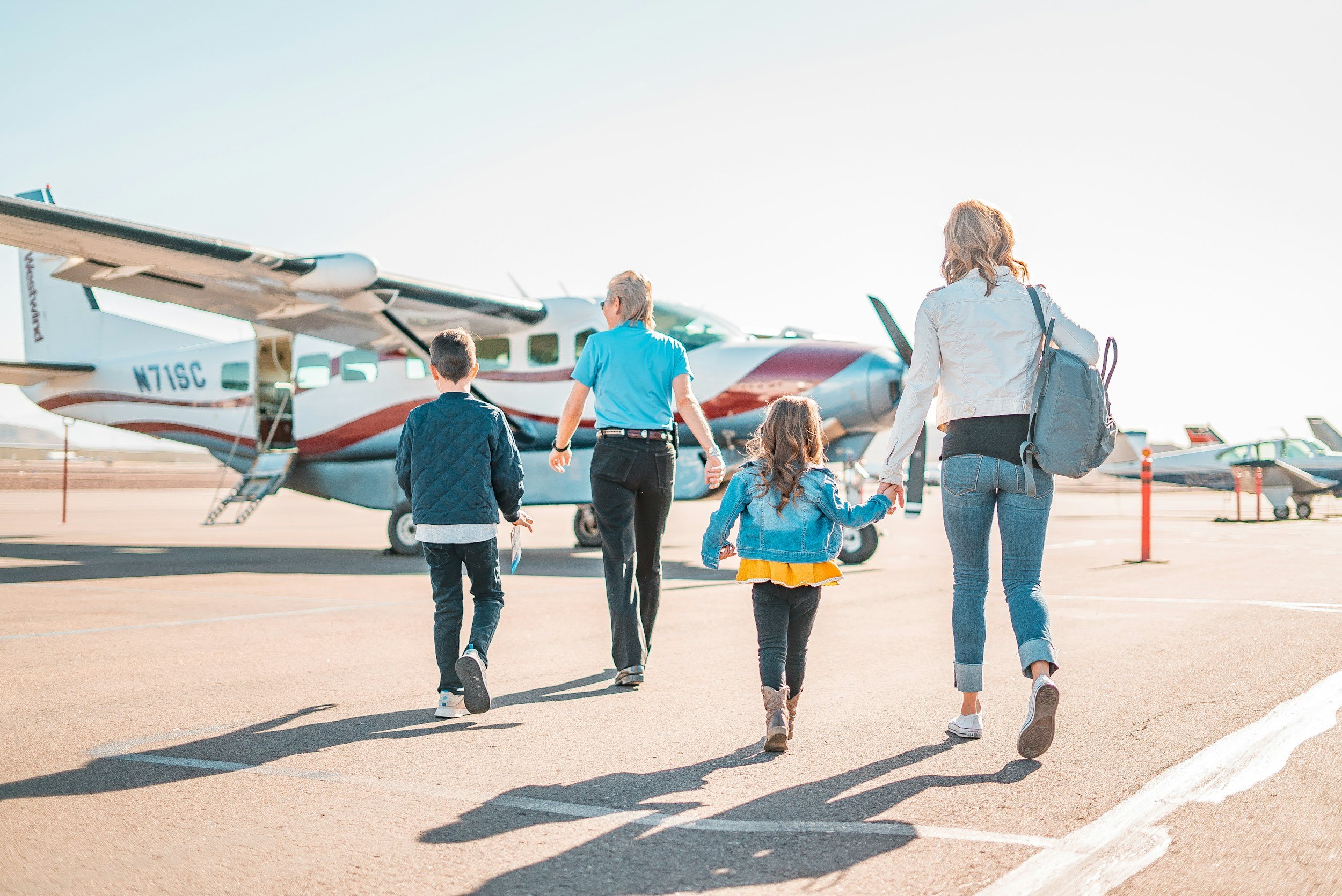 Two adults and two children walking beside private aircraft on an airport apron.