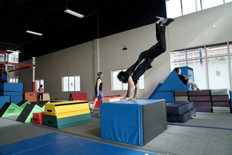 Person doing a handstand on gym mats at an indoor gym with birthday celebration decorations in the background.