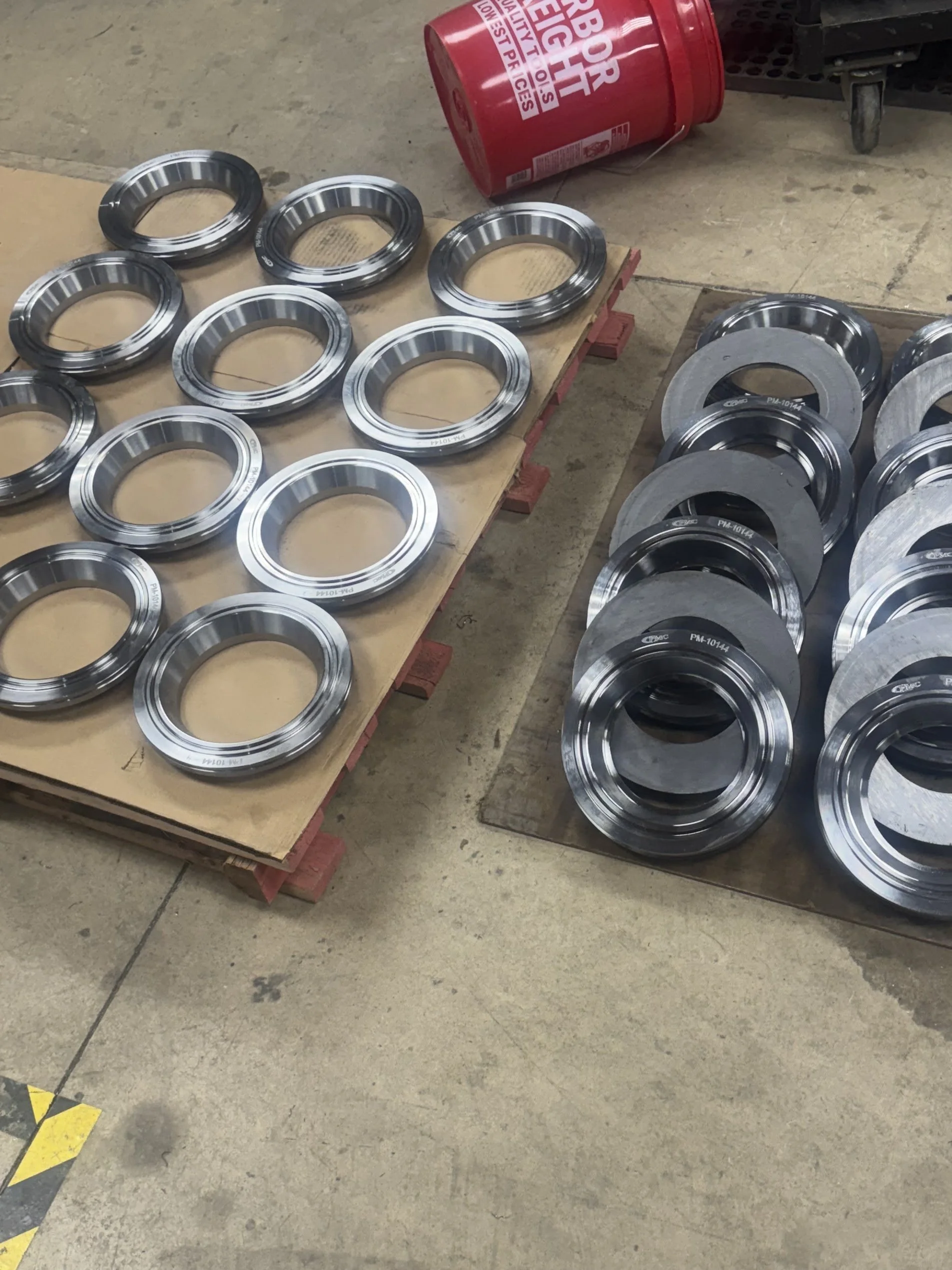 Collection of metal ball bearings and metal washers on wooden pallets and concrete floor in a warehouse or workshop setting.