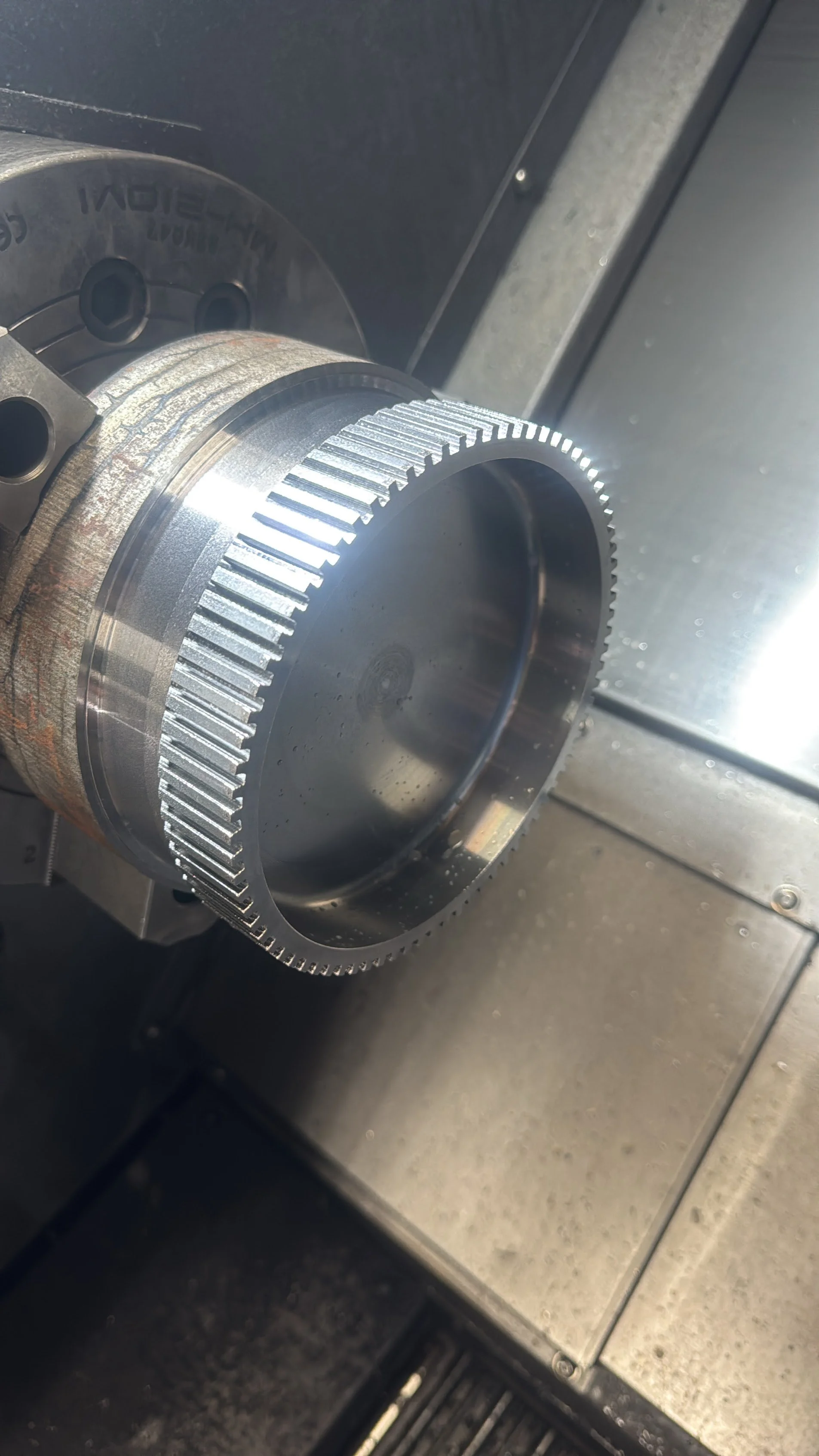 Close-up of a metal gear with gear teeth, mounted on a mechanical apparatus.