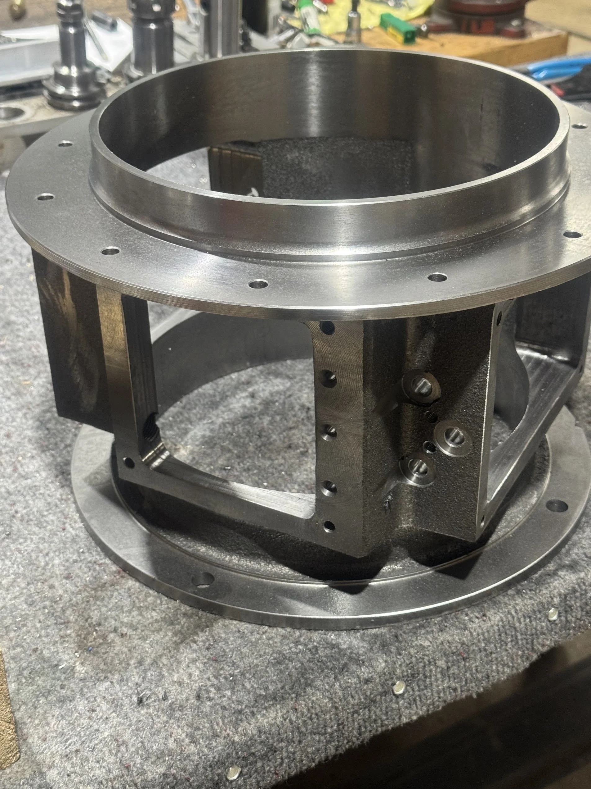 Close-up of a machined metal component with circular and rectangular features, placed on a workbench in a workshop.