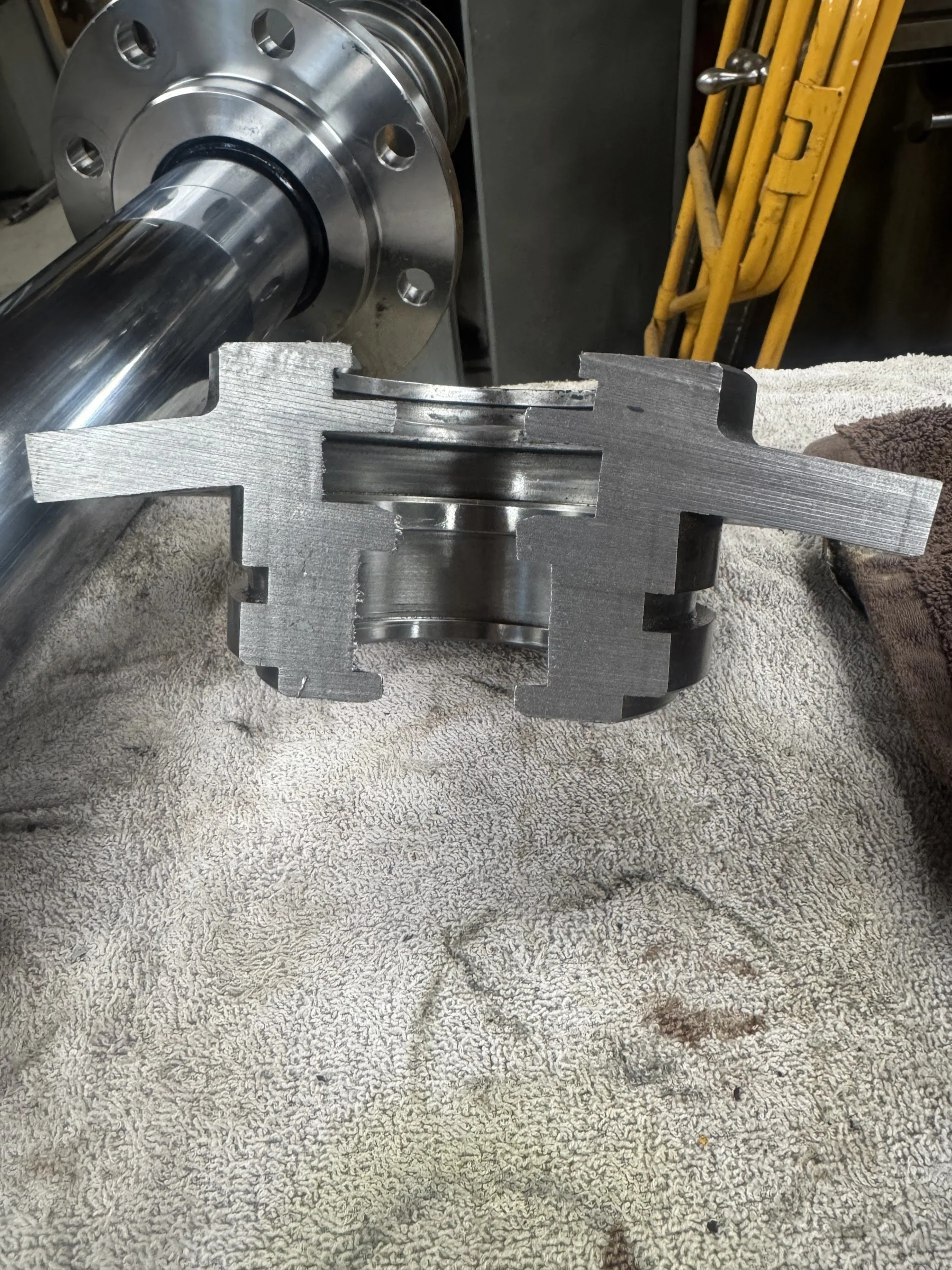 A metal gearbox with a long cylindrical shaft resting on a textured towel, with a yellow hand truck in the background.