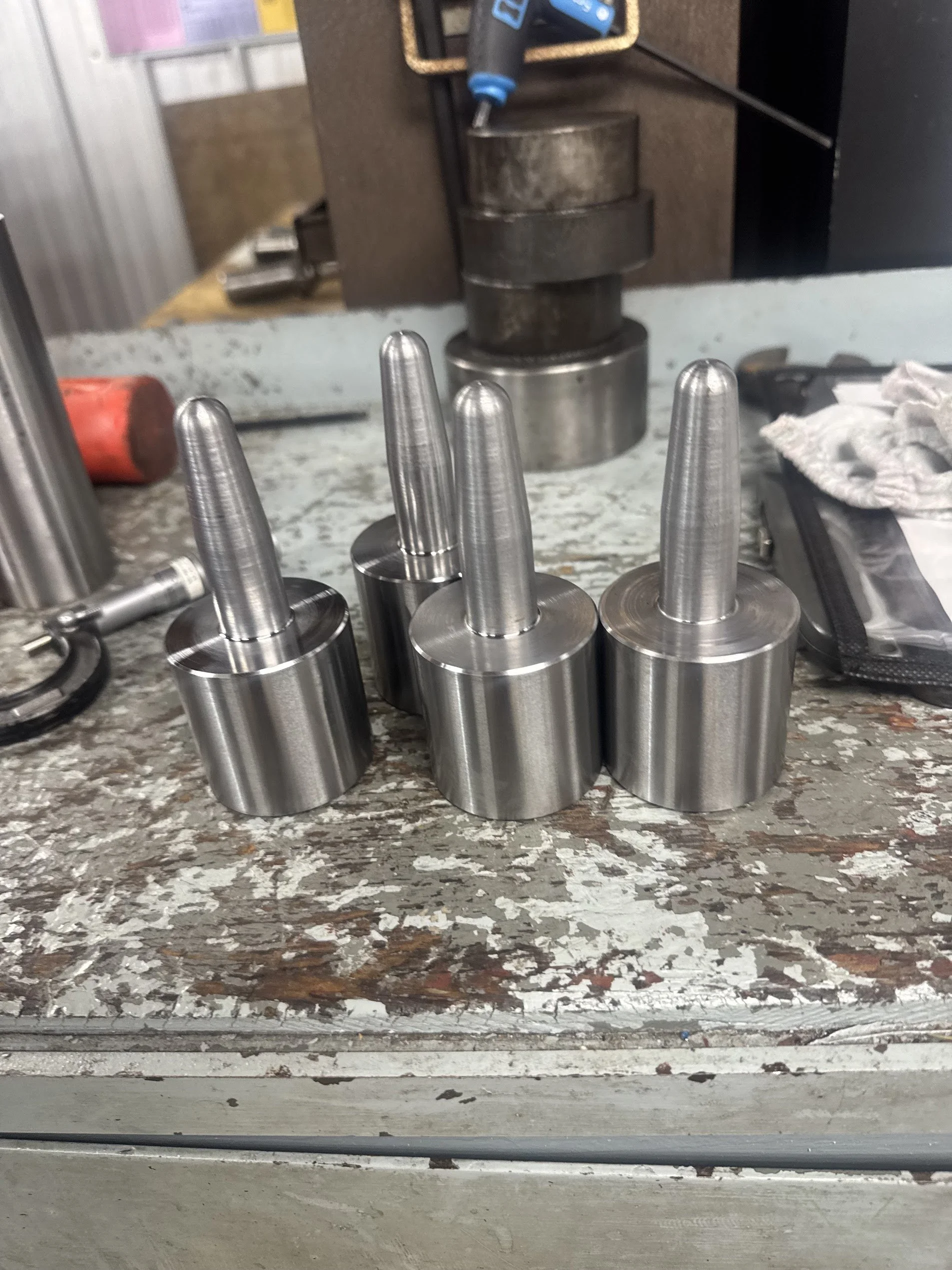 Stacked metal components on a workbench with tools and machinery in the background.
