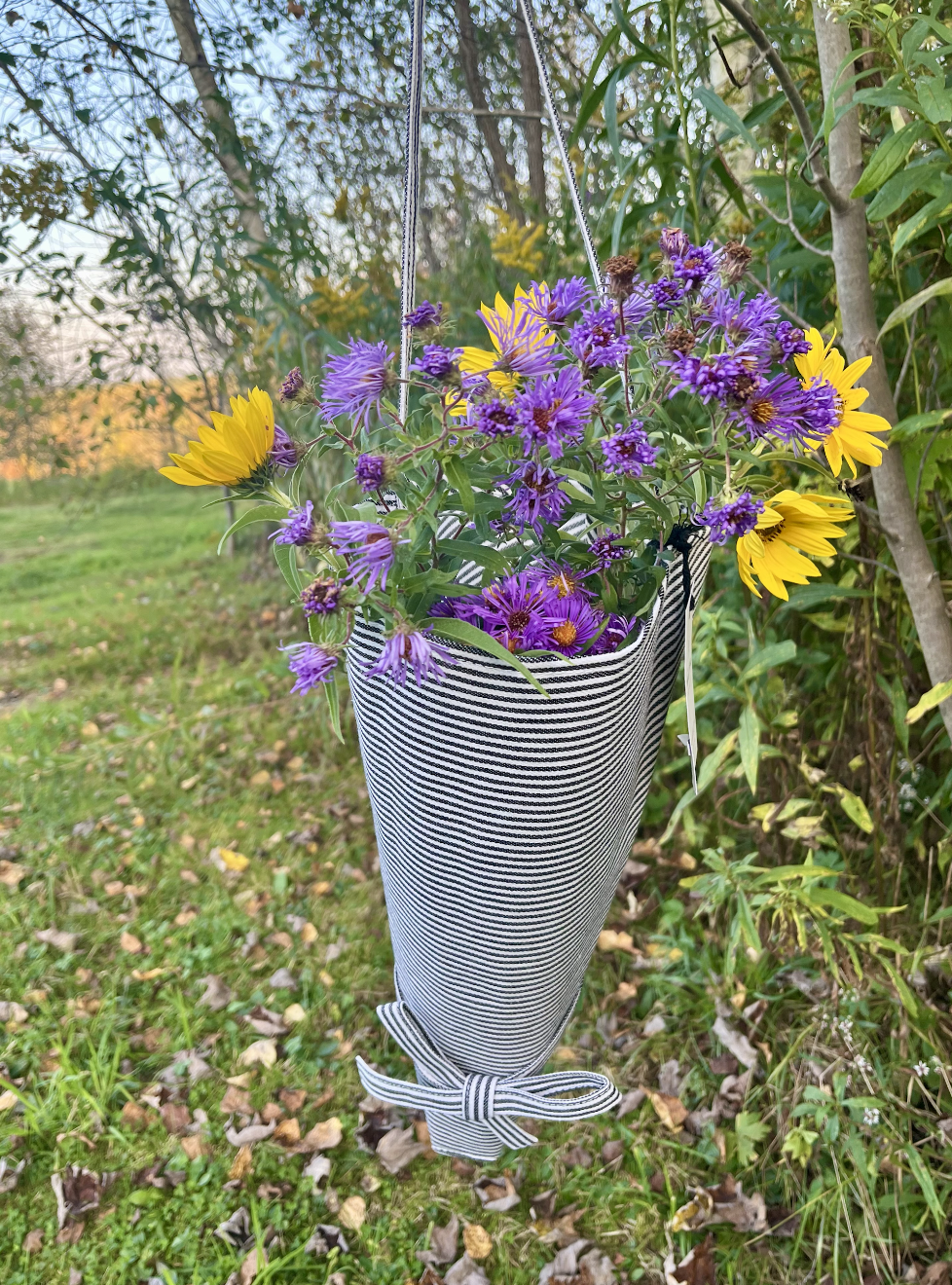 A hanging basket with purple and yellow flowers, suspended outdoors among trees and greenery.