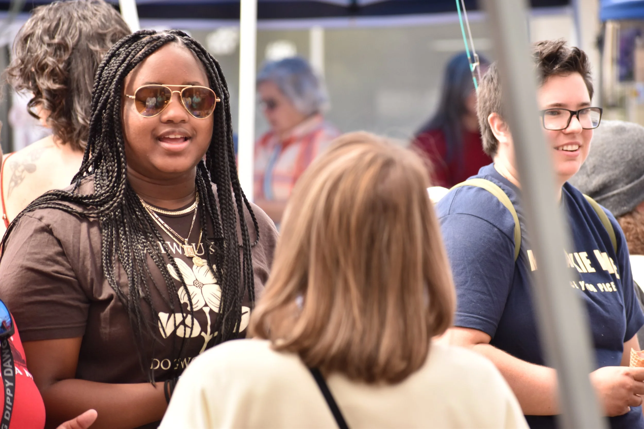 Group of diverse young people gathered outdoors at a social event, engaging in conversation and smiling.