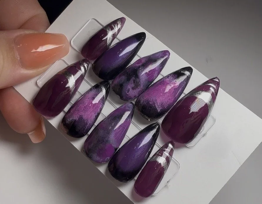 Set of ten artificial nail tips with purple, black, and white marble and striped designs, attached to a white display card.