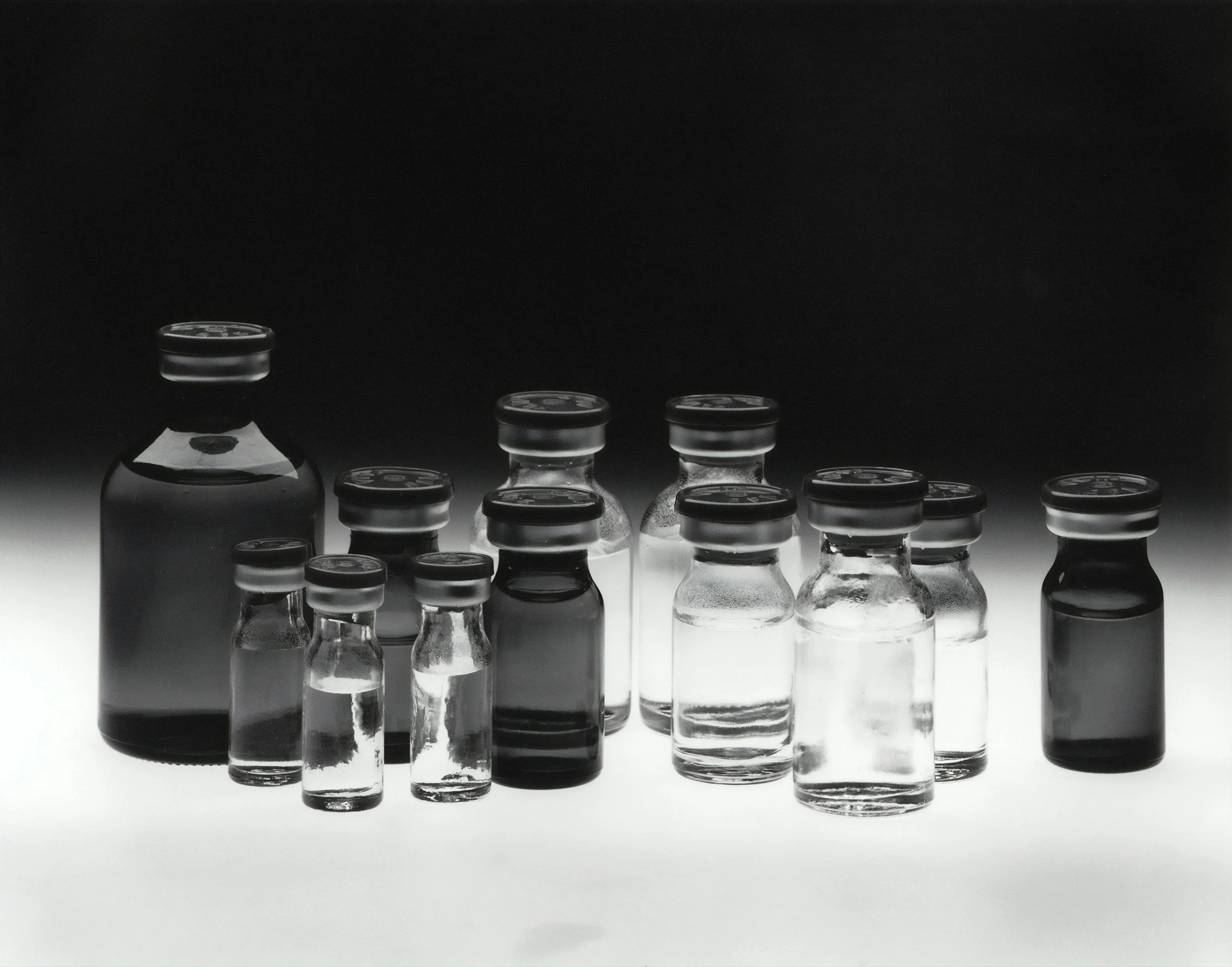 Multiple glass vials with black caps arranged on a white surface against a black background.