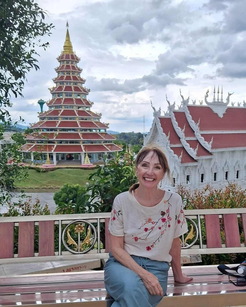 Sandy seated in front of an ornate Buddhist temple in Chiang Rai, Thailand.