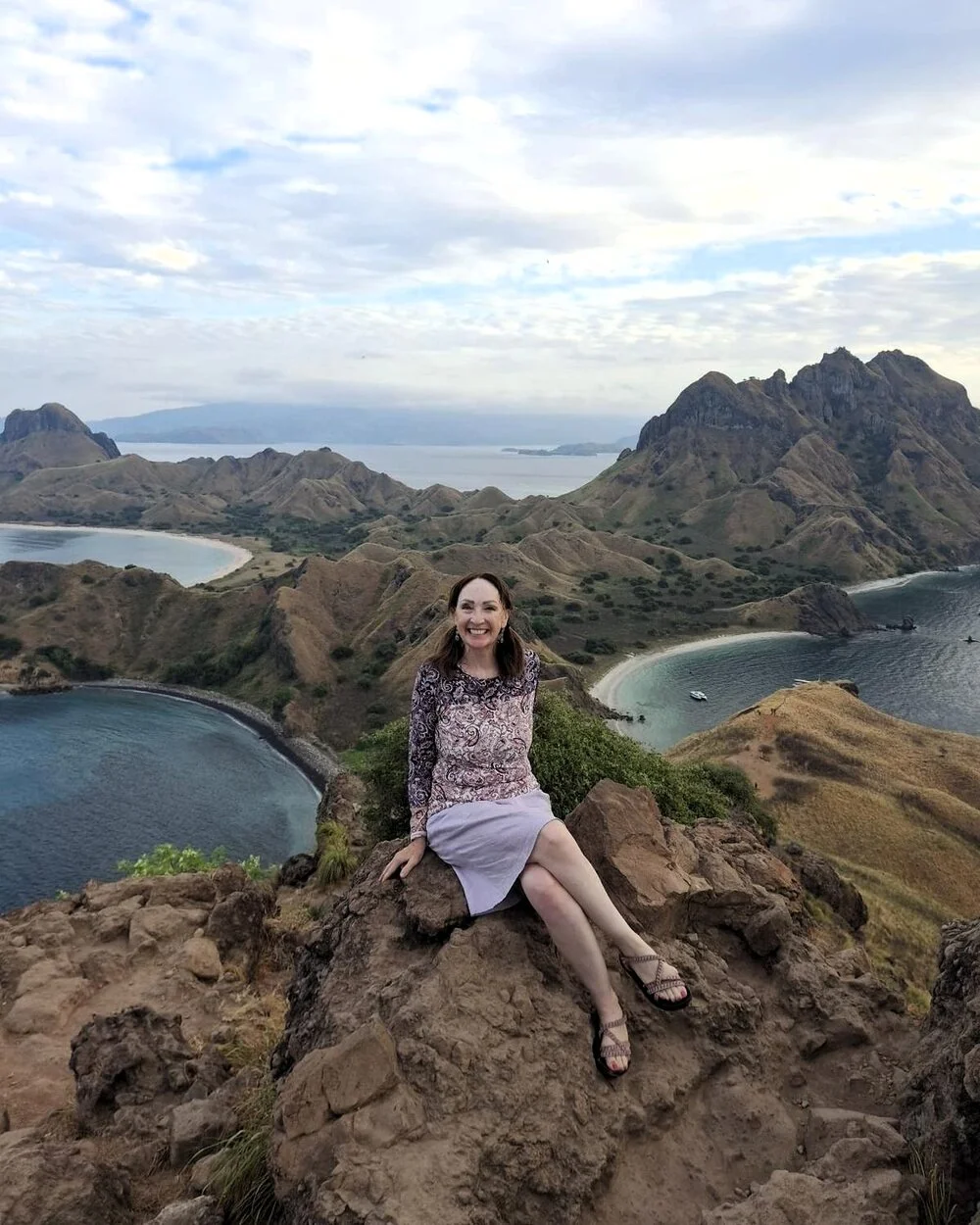 Woman sitting at a scenic overlook above rugged islands and blue ocean in Komodo National Park, Indonesia