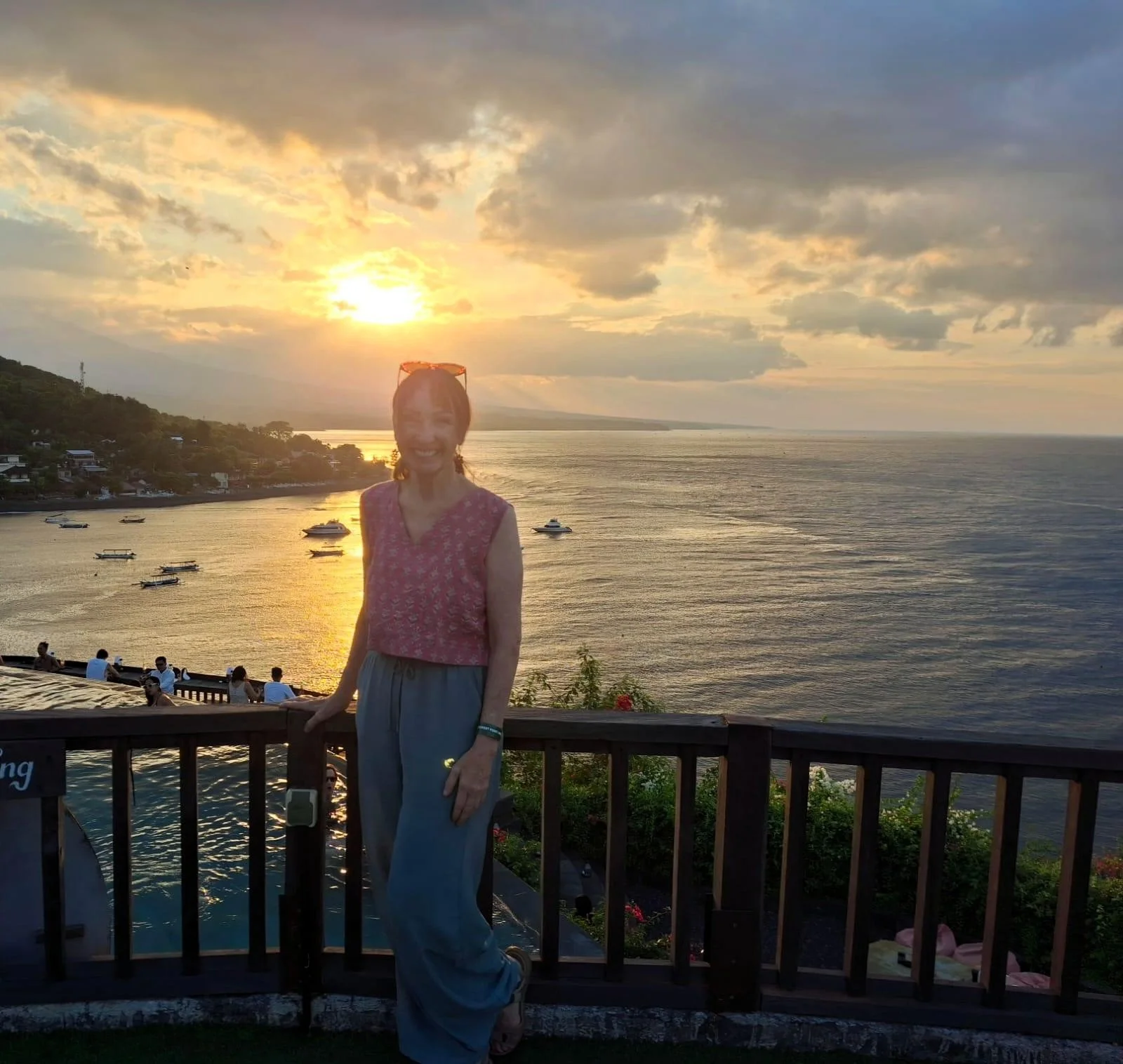 Woman standing on a balcony overlooking the ocean at sunset in Bali, Indonesia