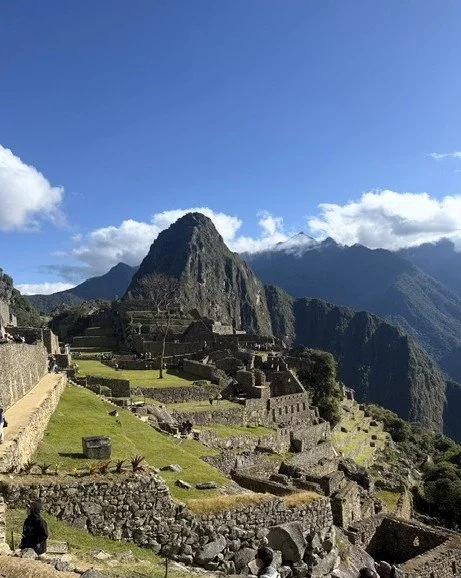 Machu Picchu ruins surrounded by the Andes Mountains under a blue sky in Peru.