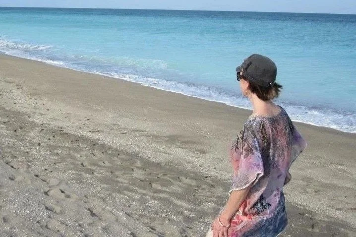 Woman walking along a quiet beach and looking out toward the ocean
