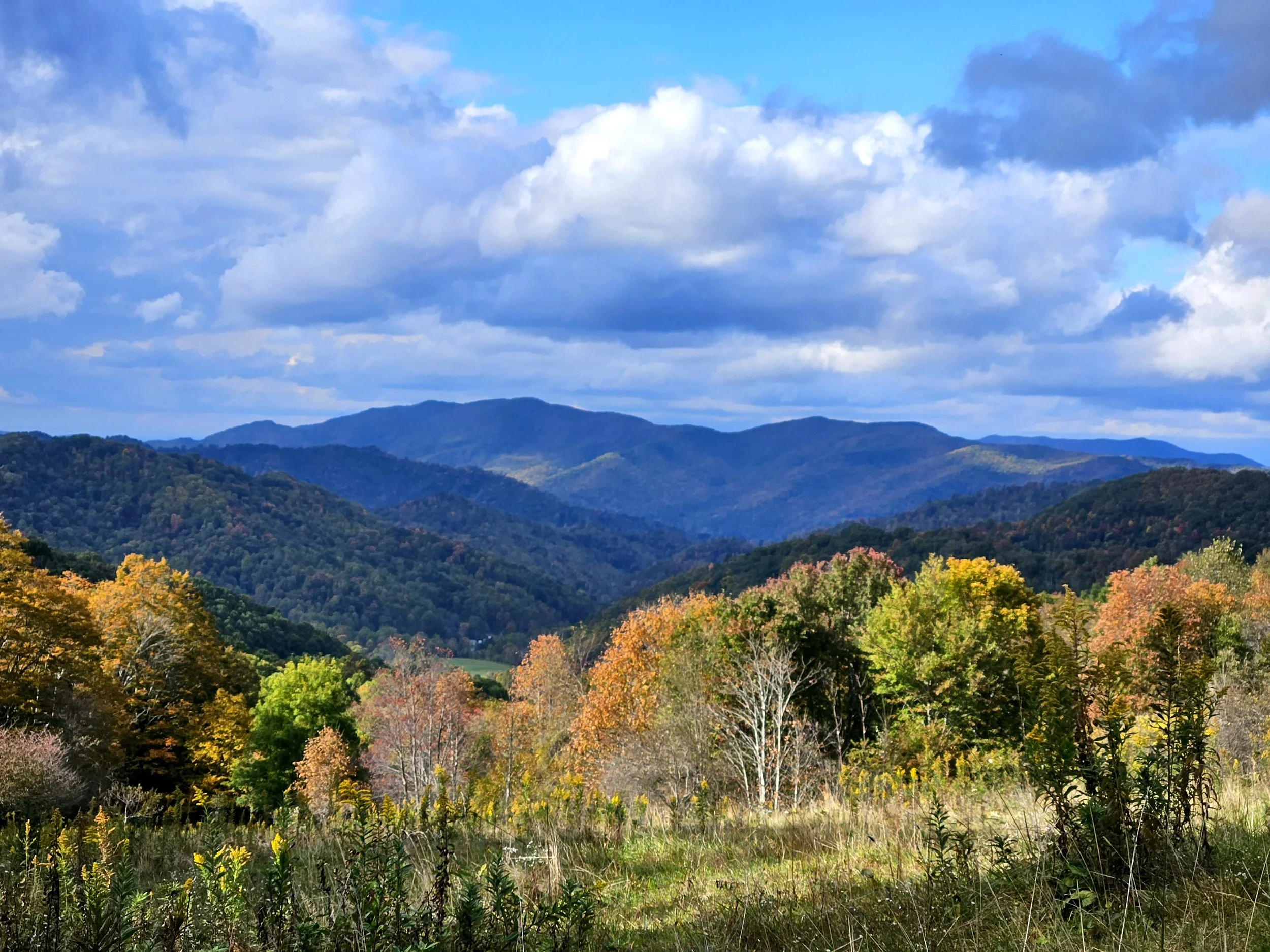 Scenic view of rolling hills and mountains with a partly cloudy blue sky.