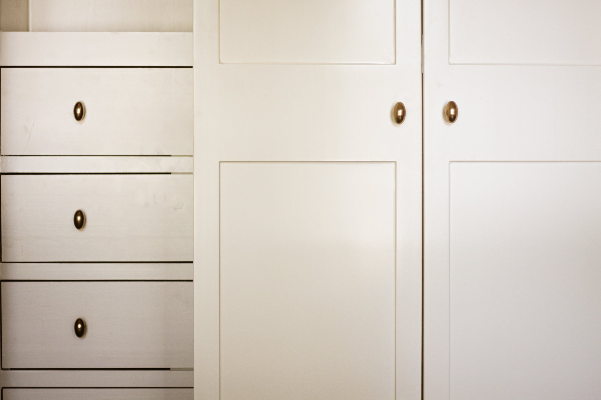 Close-up of white wooden furniture with drawers and cabinet doors, featuring bronze-colored knobs.