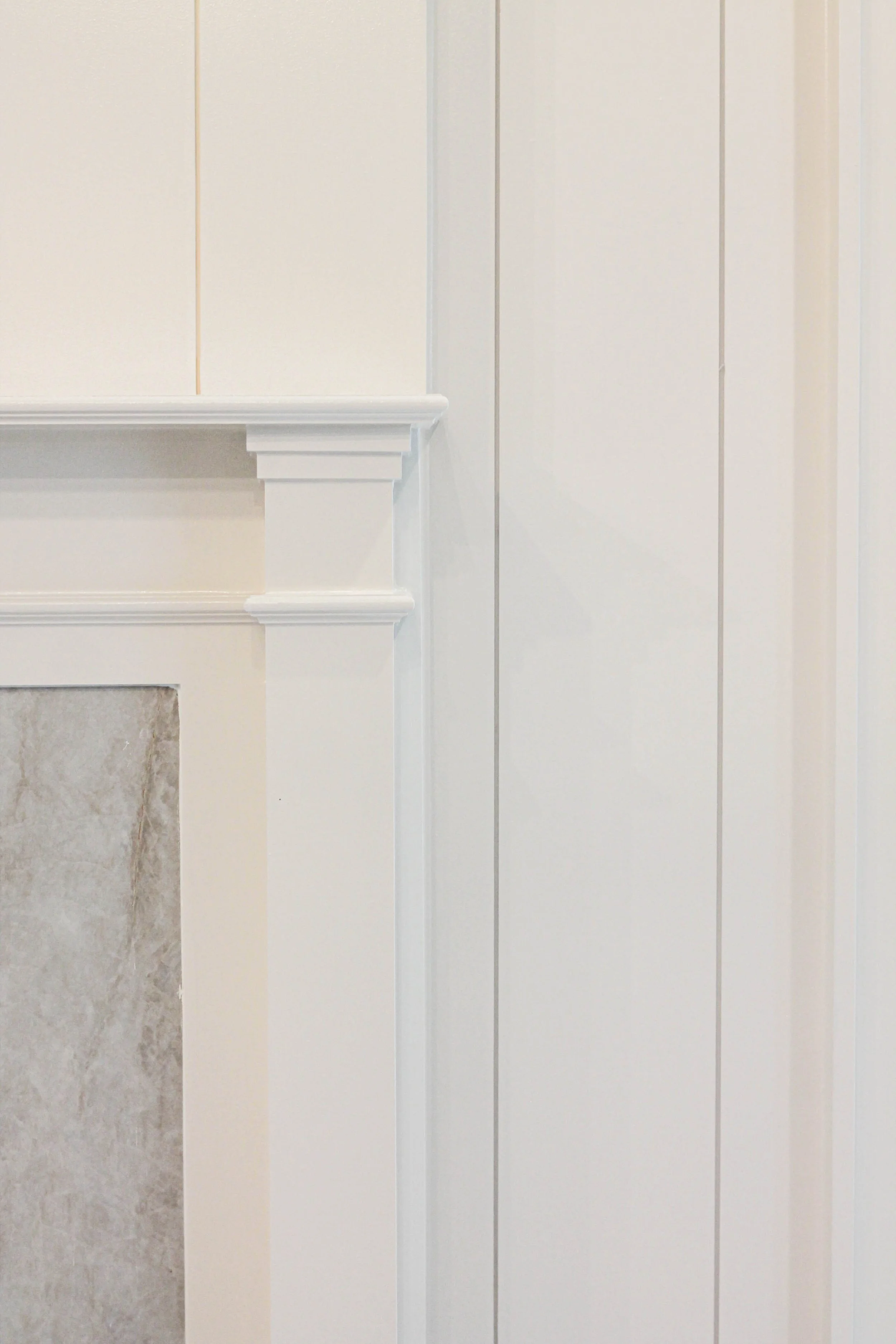 Close-up of a white wooden fireplace mantel with vertical wall paneling in the background.