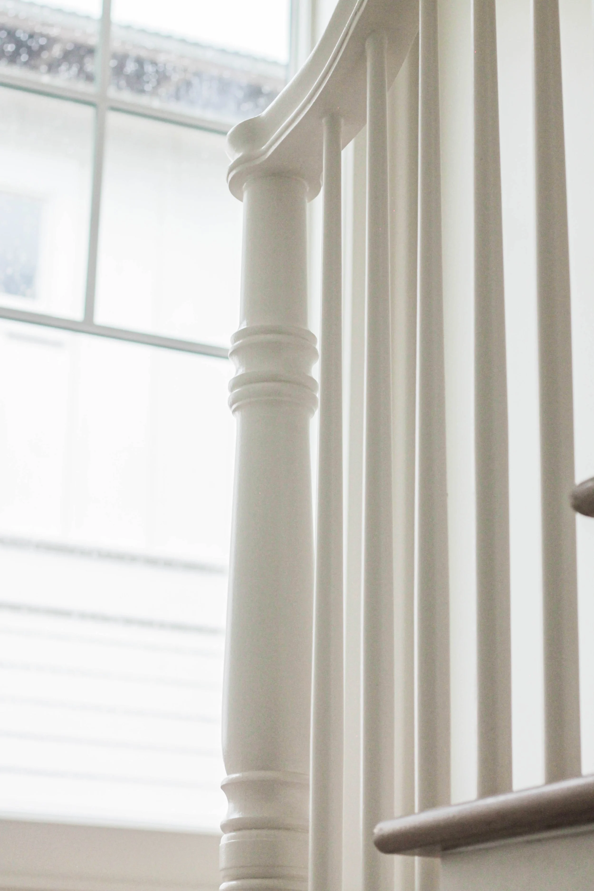 Close-up of a white wooden staircase railing near a window with natural light coming through.