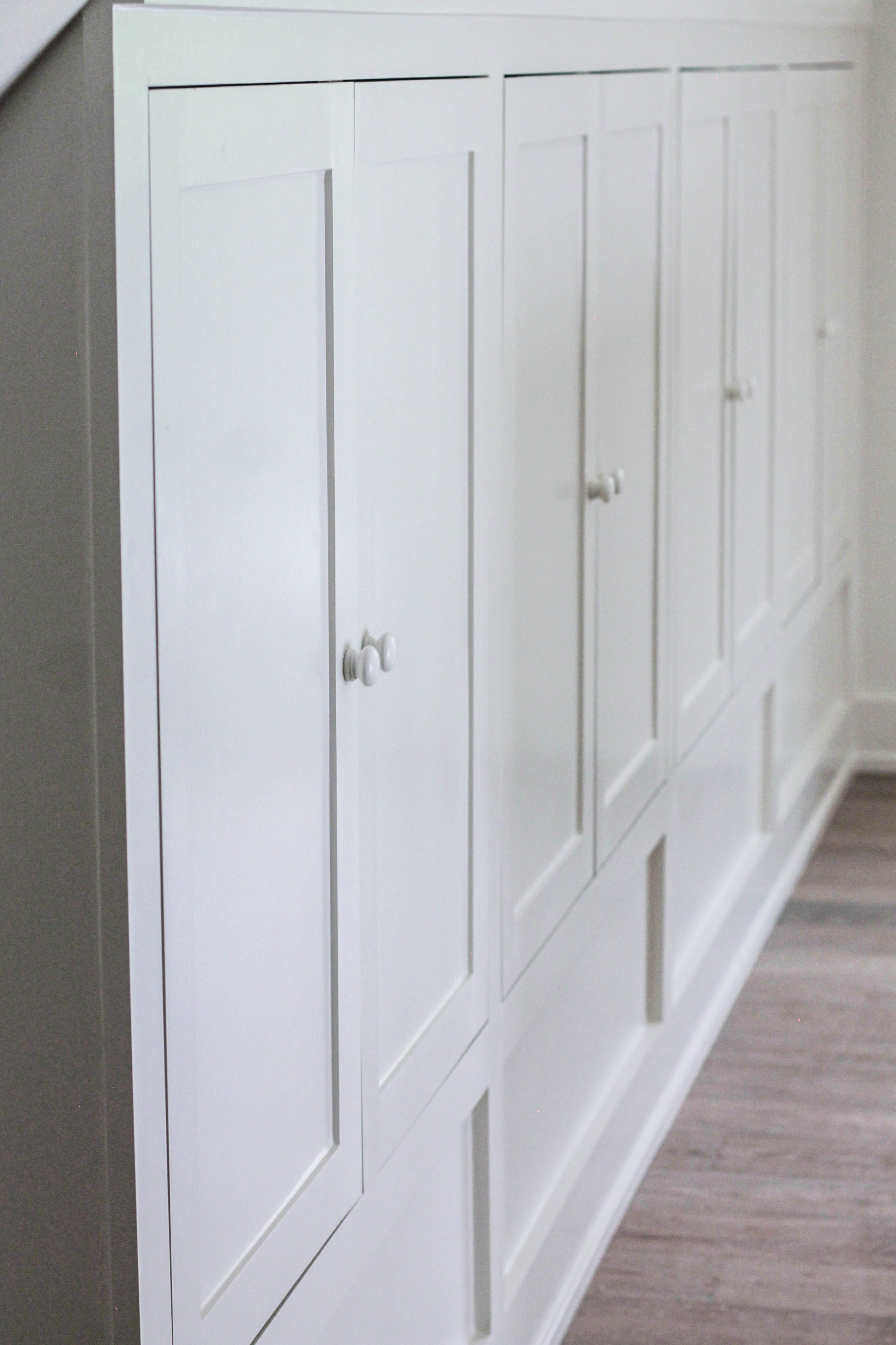 White cabinet with multiple doors and round knobs, against a wall with grey baseboard and floor.
