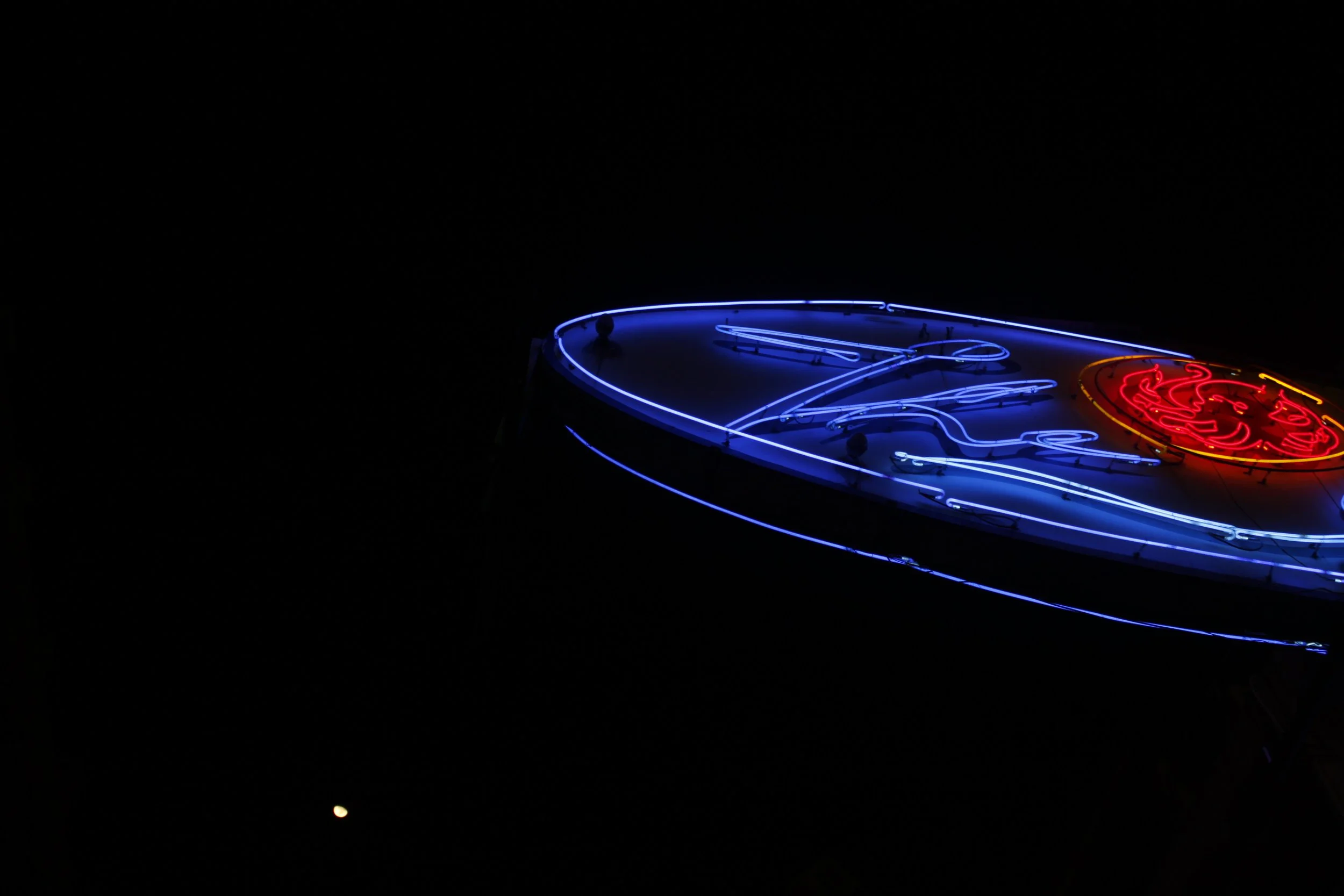 Neon sign with blue, red, and yellow colors glowing in the dark, partially visible.