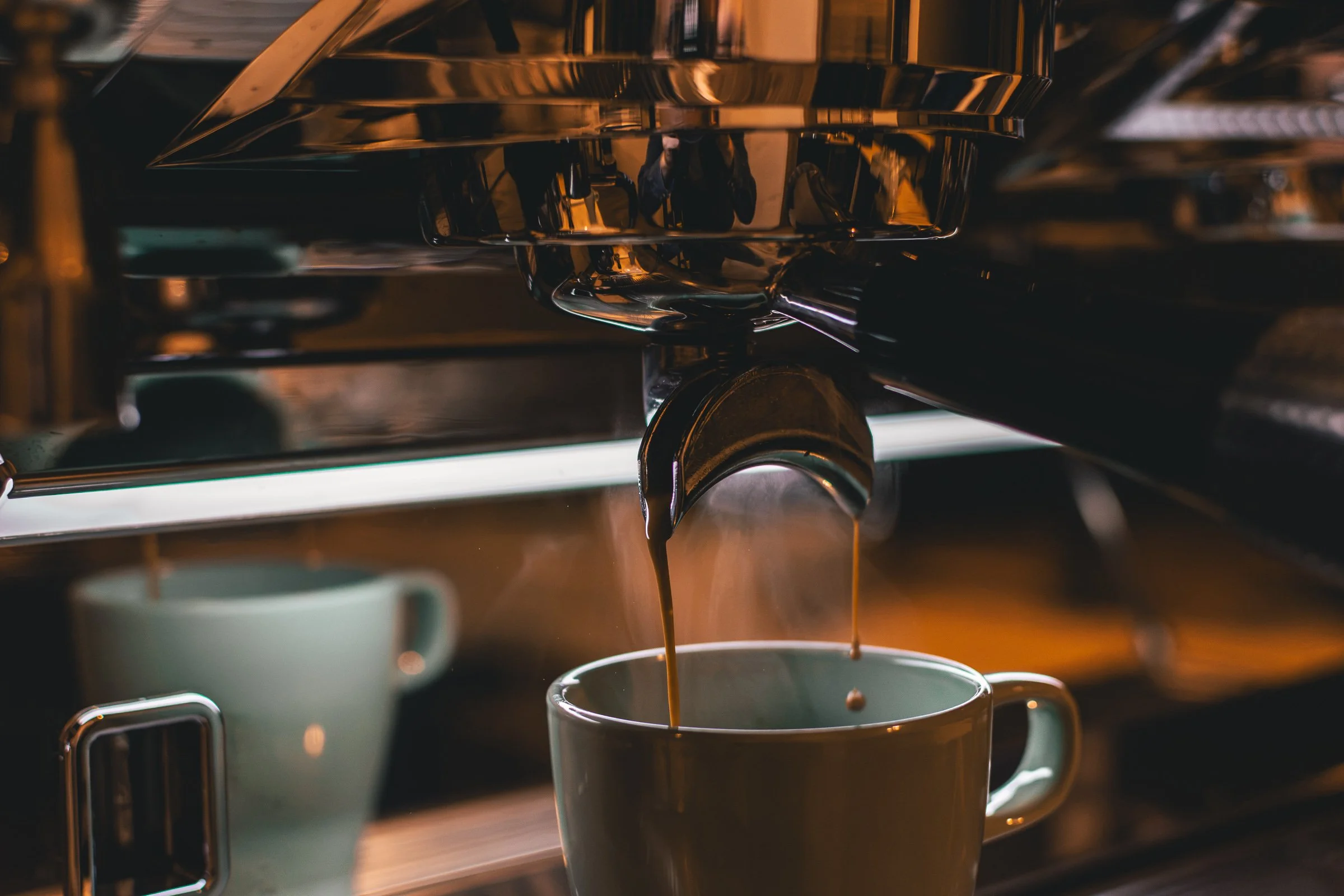 Hot coffee being poured from a espresso machine into white mugs.