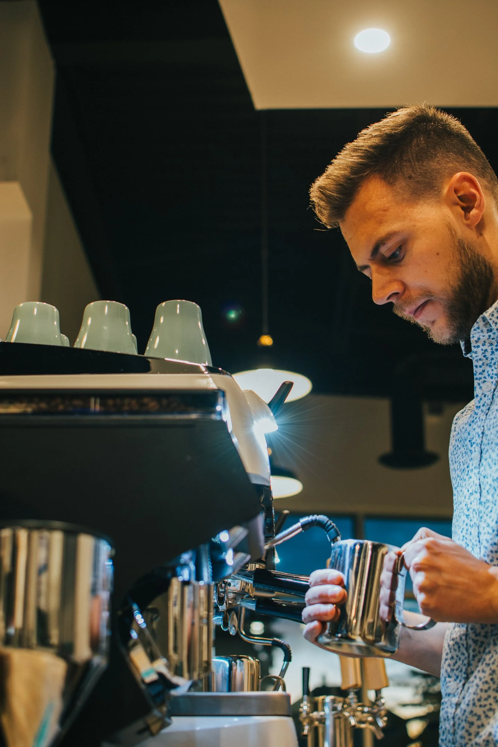 A barista making espresso behind the counter at a coffee shop.