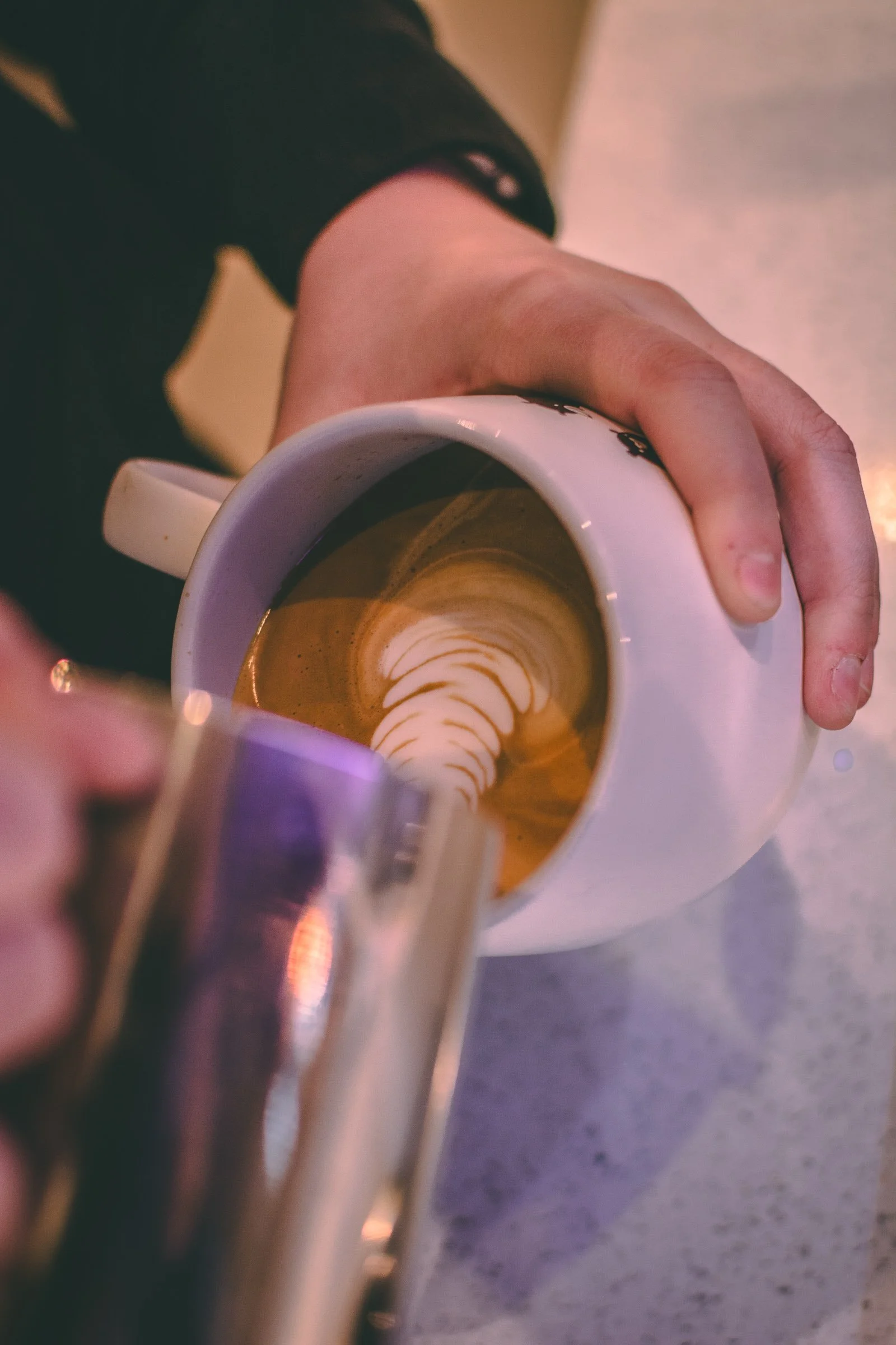 Close-up of a person's hand holding a white ceramic coffee cup filled with coffee, with latte art visible on the surface.