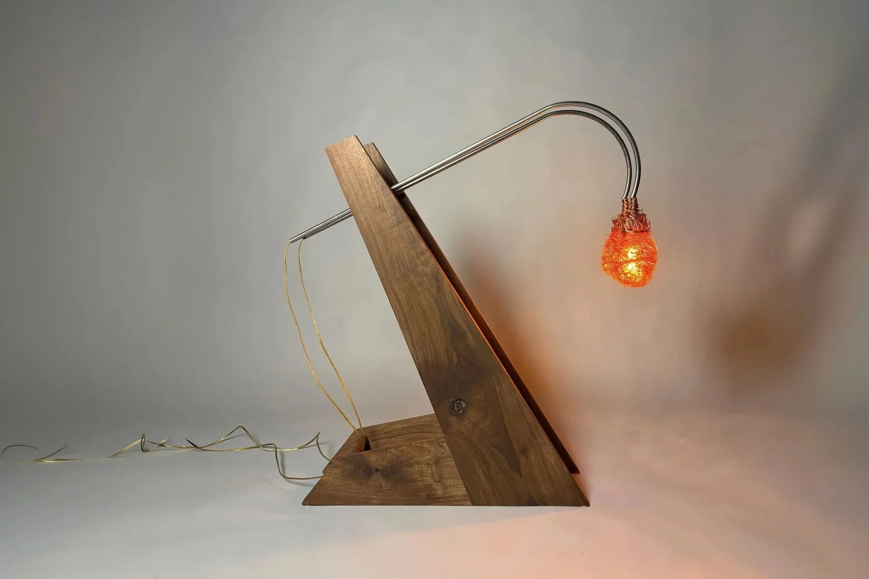 A modern desk lamp with a wooden base, a curved metal arm, and an illuminated orange filament bulb, set against a plain background.