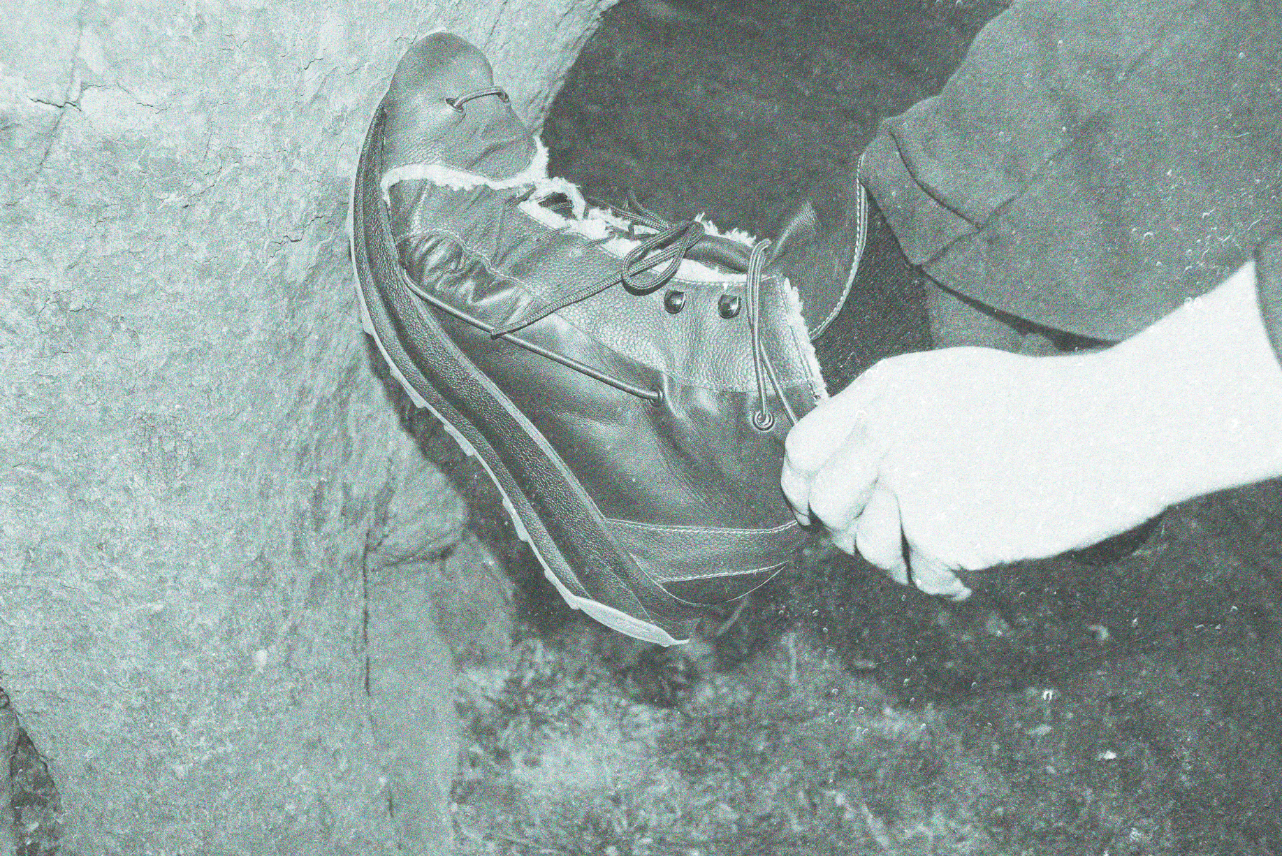 A person with gloves lacing up a hiking boot on a rough concrete ground.