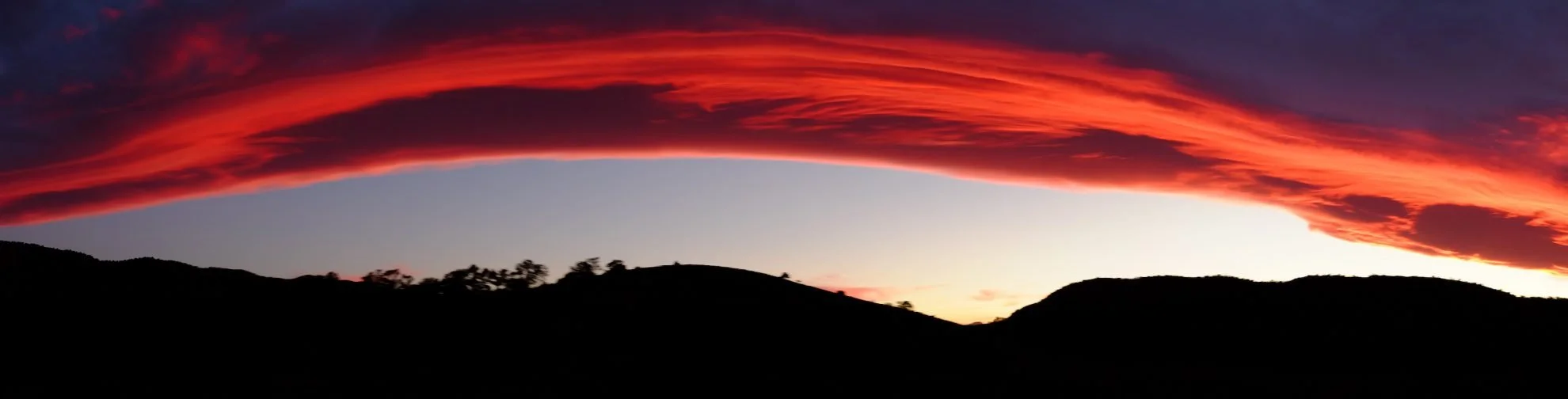 Sunset with vibrant red and orange clouds over silhouetted hills.