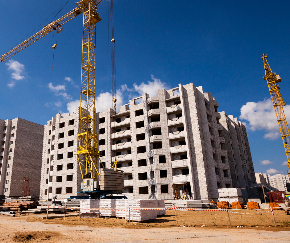 Construction site with a multi-story building under construction, yellow cranes, and building materials on the ground.