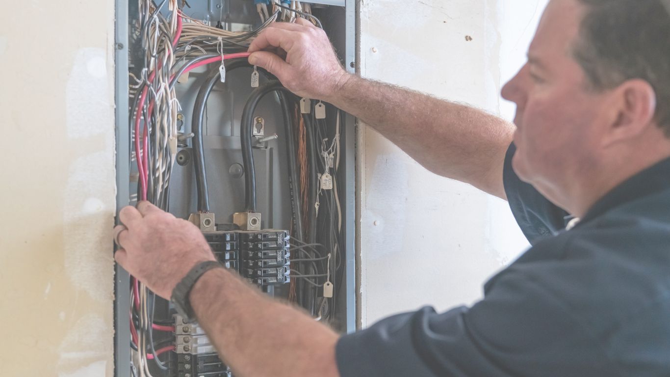 A man working on an electrical panel, handling wires inside an open electrical cabinet.