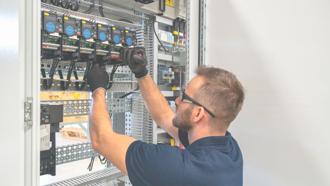 A technician working on an electrical control panel, wearing safety glasses and black gloves.