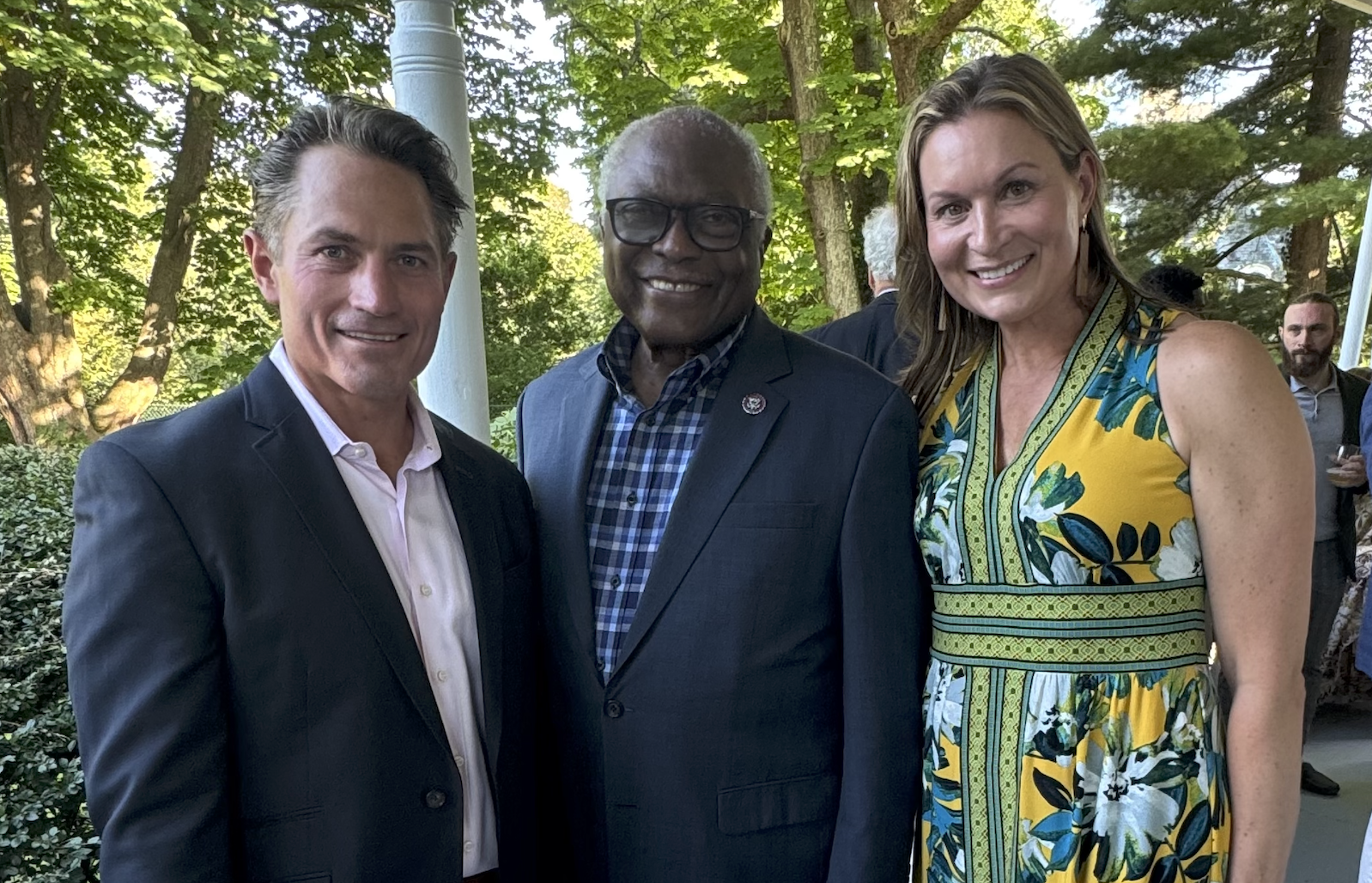 Three people standing outdoors, smiling, with trees and foliage in the background. On the left is Dr. Fred Hartman, center is U.S. Senator James Clyborn, and right is Neile Hartman, candidate for Barrington Town Council.
