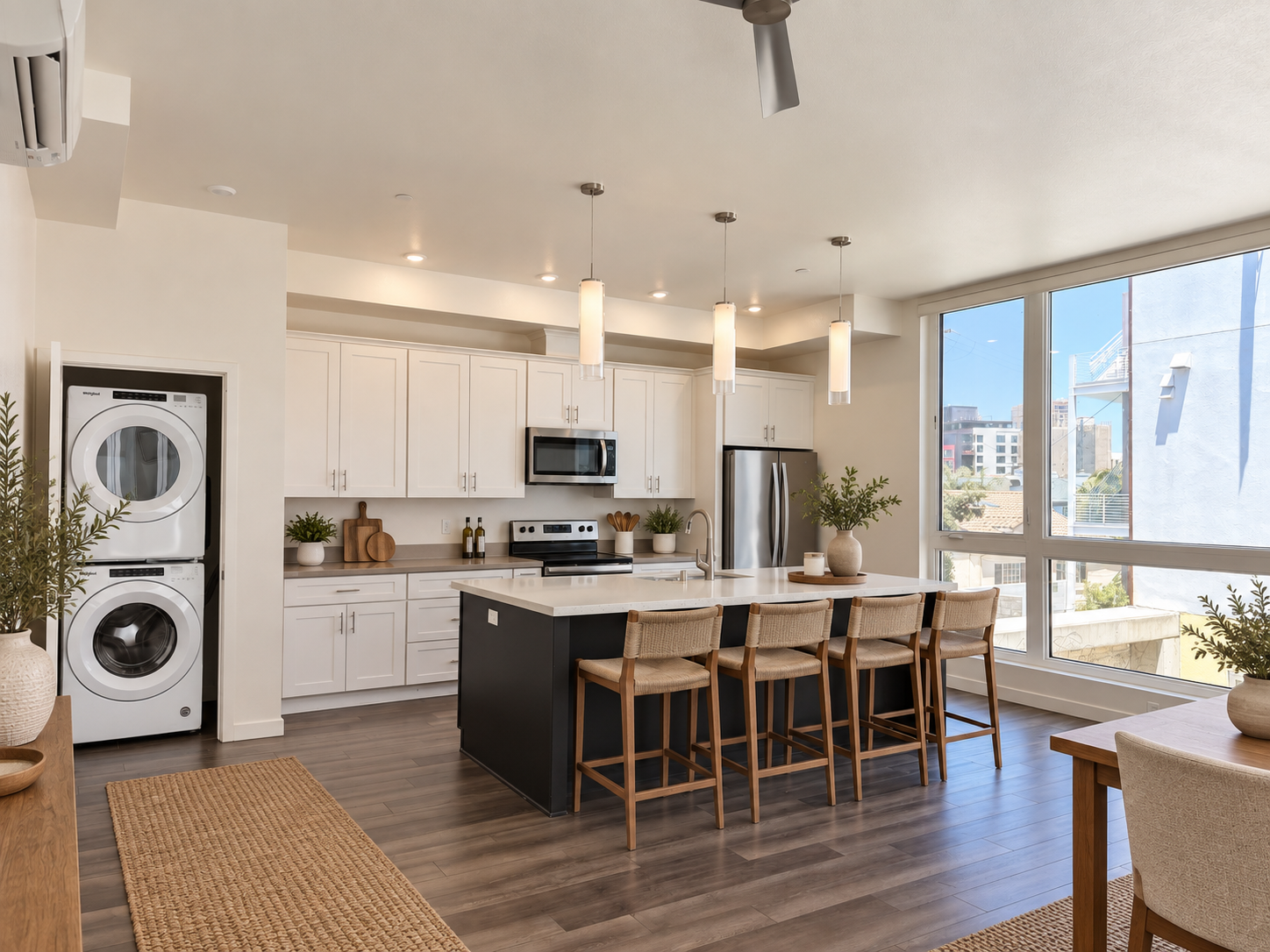 Modern kitchen with white cabinets, a black island, three wooden bar stools, stainless steel appliances, large windows, and potted plants.