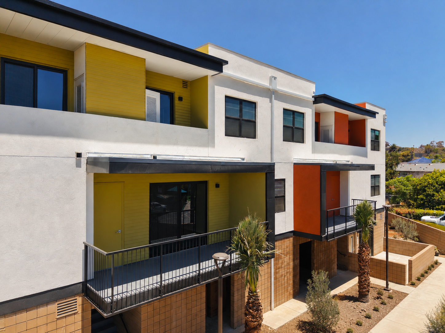 Modern multi-story apartment building with colorful exterior panels, balconies, and desert landscaping including palm trees.