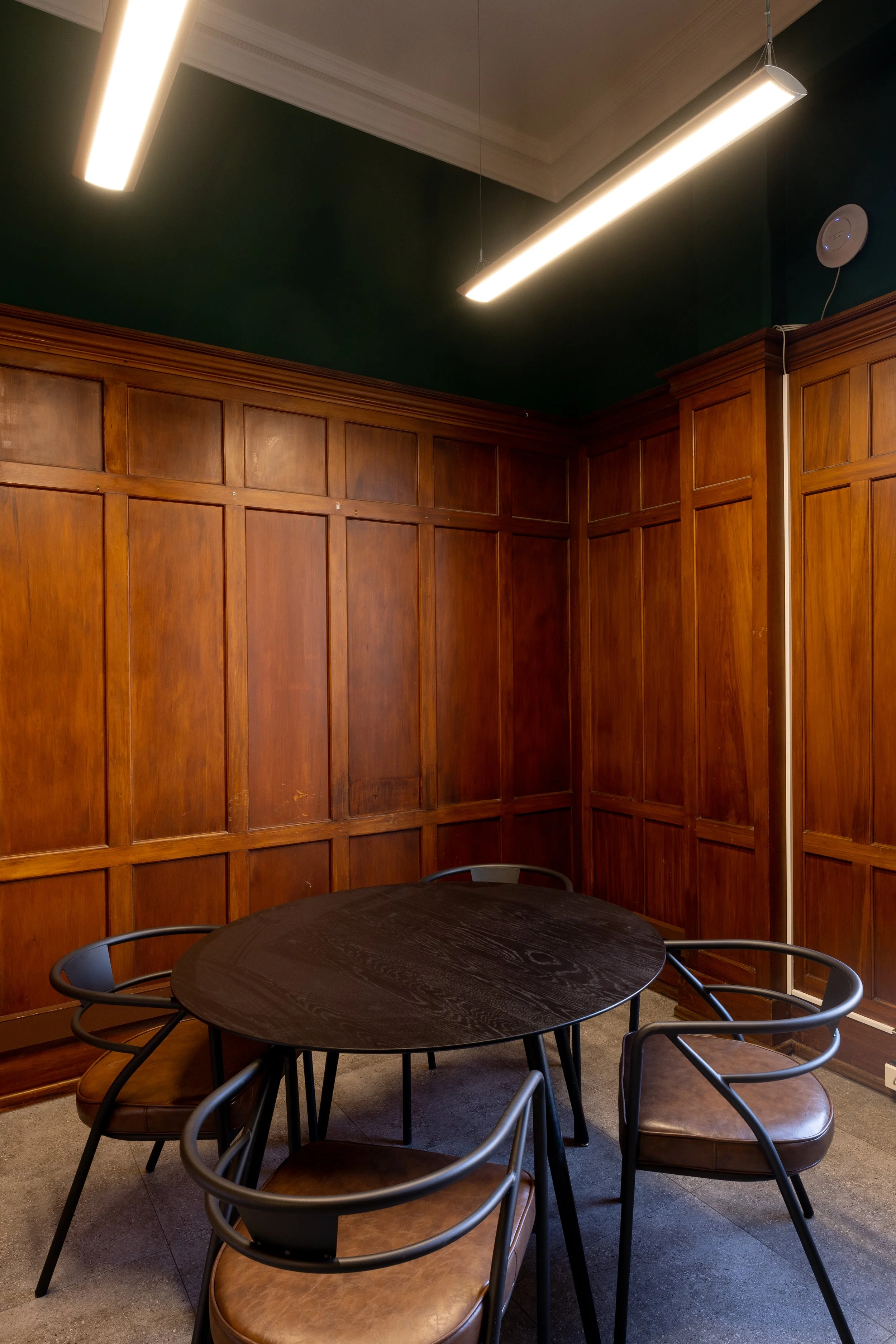 A small private meeting room with interior wood-panelling, a large window, and a modern ceiling light. Bookable meeting room via the Bad Company website. Meeting room based at Bad Company Hawkes Bay, in Hastings, New Zealand. 
