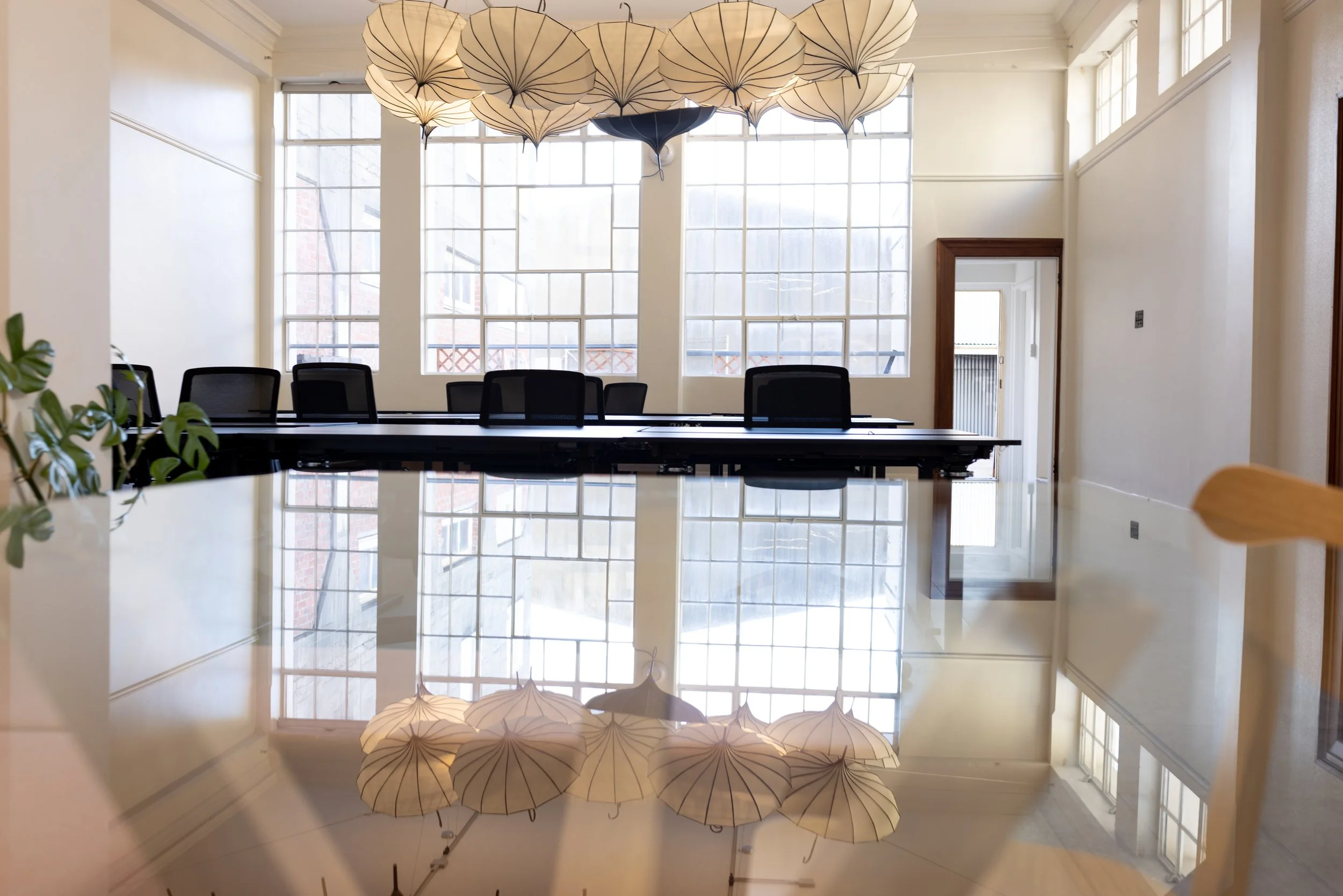 Interior of a bright, modern coworking space with black chairs, and decorative umbrella-shaped light fixtures hanging from the ceiling. Large windows let in natural light, at Bad Company Hawkes Bay, a co-working space in Hastings, NZ. 