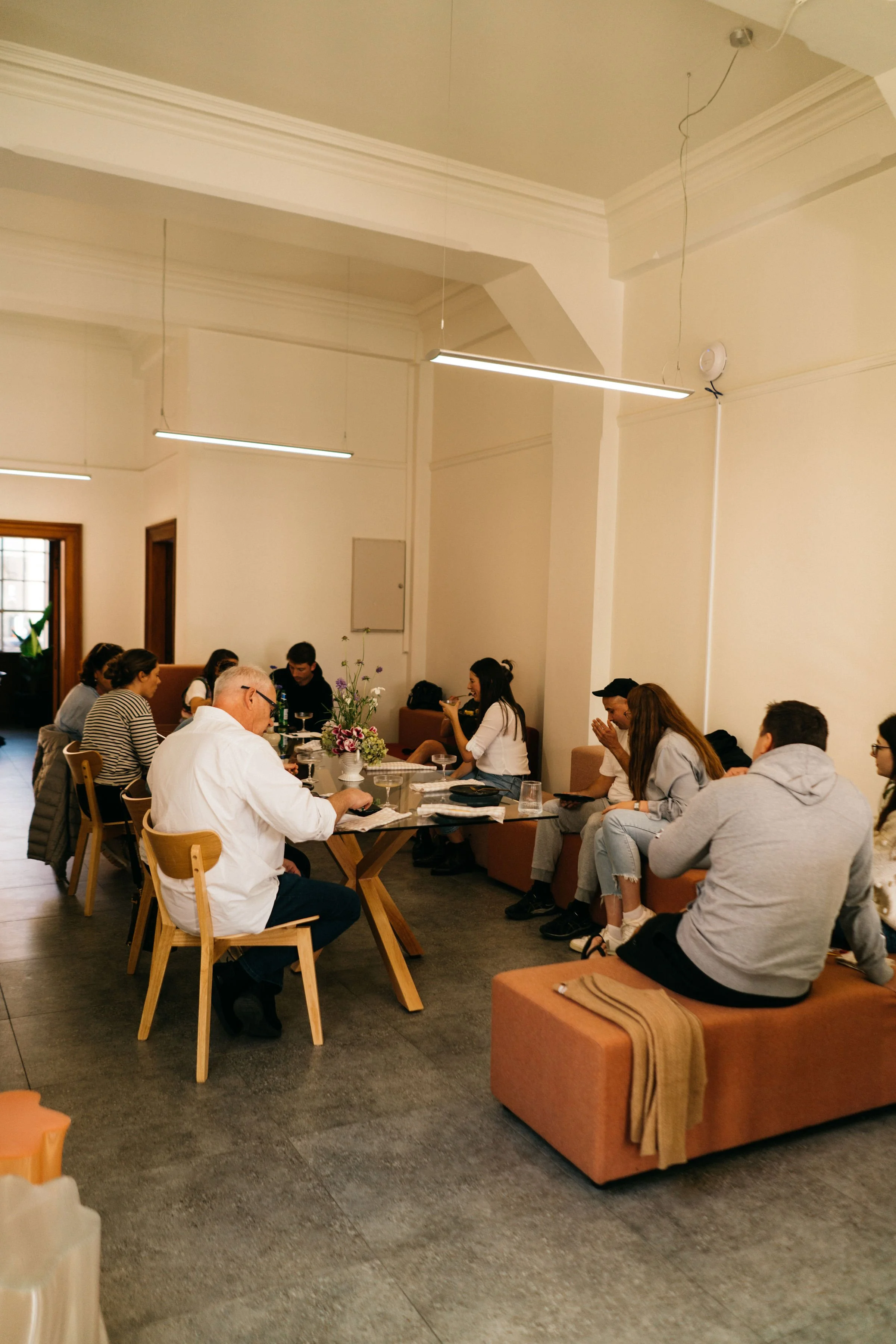 People gathered around a long table in a room, engaged in a meeting or discussion. Some are seated on chairs, others on cushioned benches at an Event at Bad Company Hawkes Bay. 