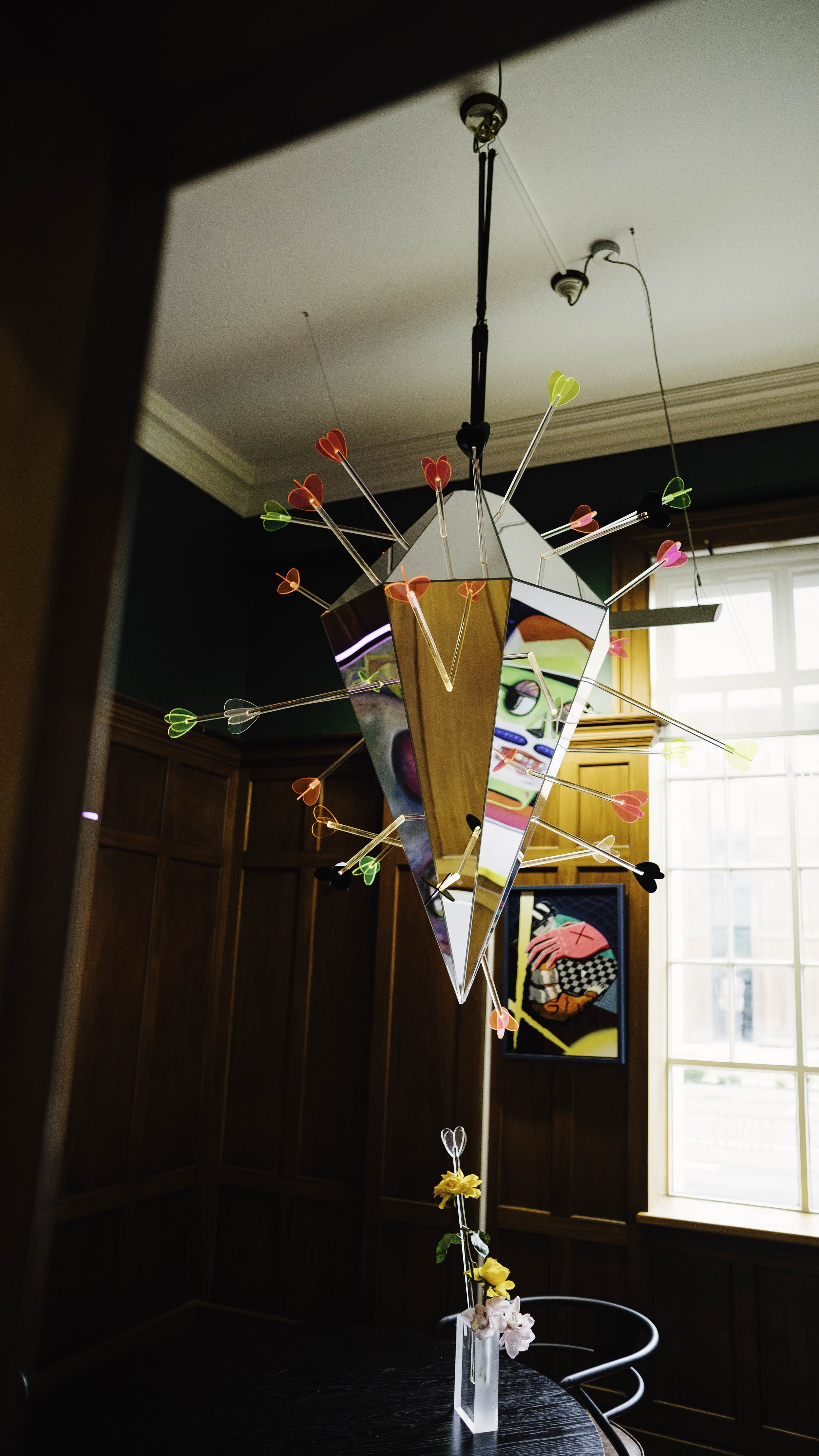 Colorful, modern chandelier with heart-shaped decorations hanging from thin sticks. The chandelier is suspended from the ceiling in a room at Bad Company Hawkes Bay. This art installation was completed by Monday Painter. 