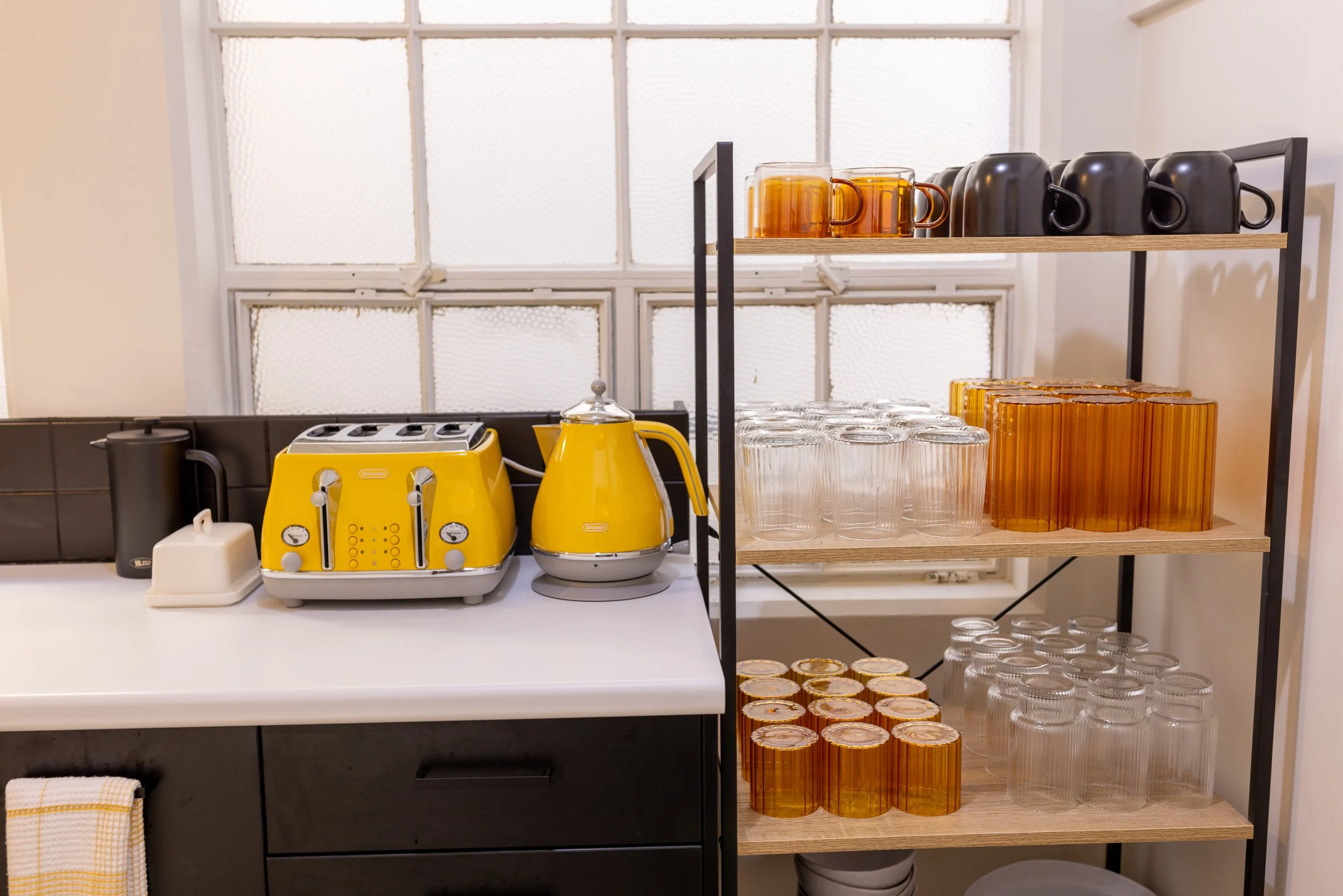 Communal kitchen shelf in Bad Company Hawkes Bay Co-working space. Amber coloured cups and black mugs for drinking a rage of tea and coffee. 