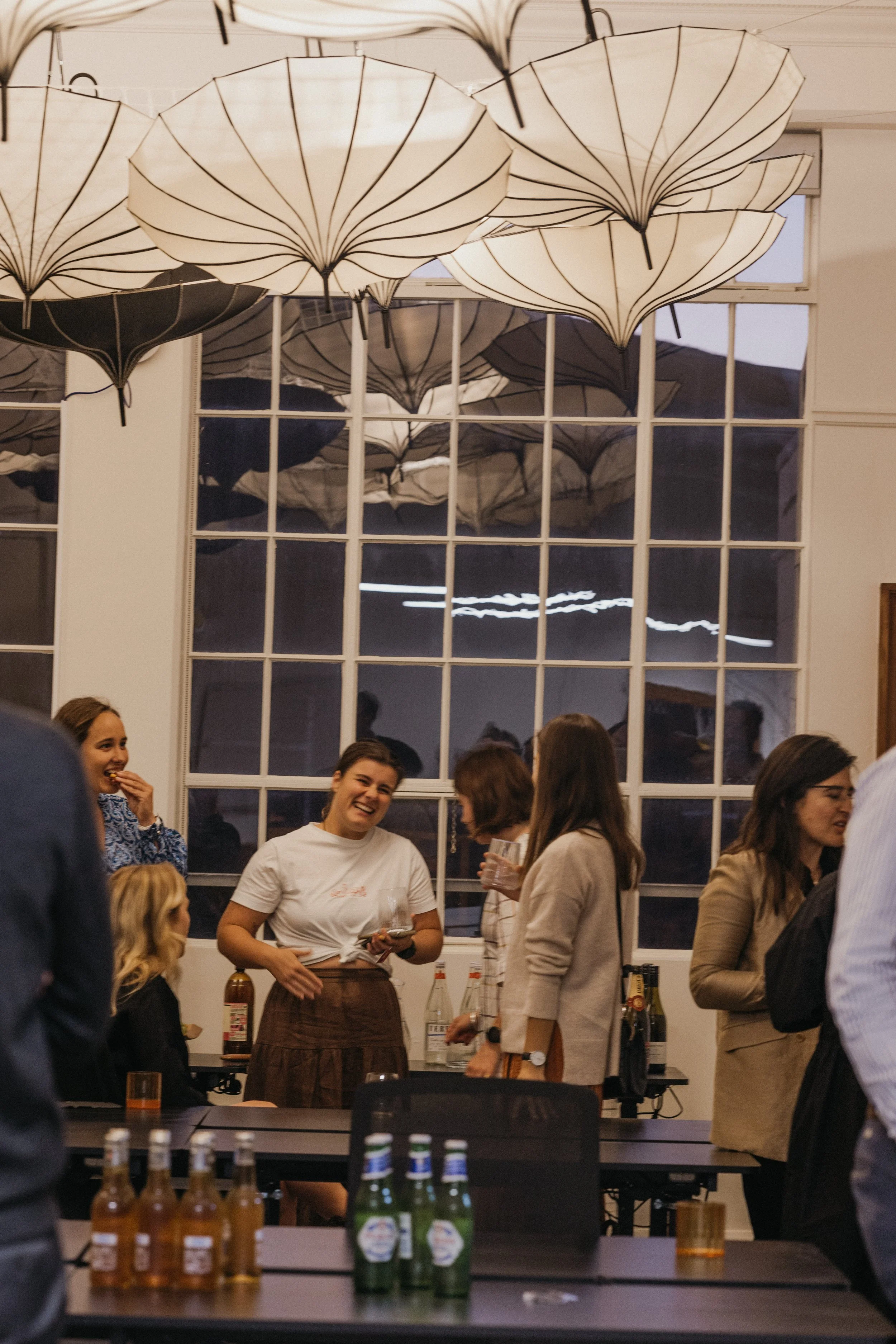Group of people socializing at a party in a room with large windows and white umbrellas hanging from the ceiling. This was an event held at Bad Company Hawkes Bay, a co-working space based in Hastings, New Zealand. 