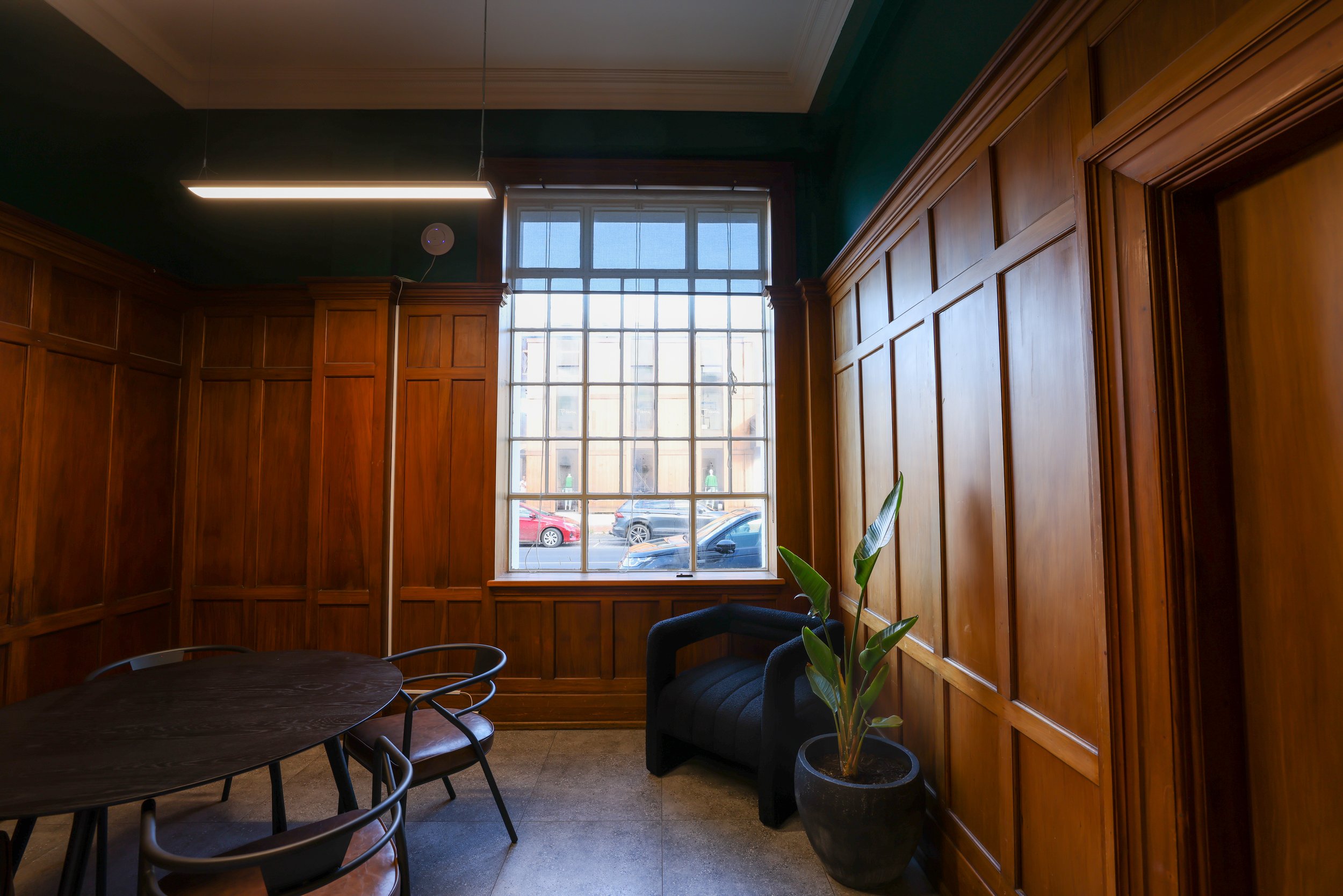 Private meeting room with interior wood-panelling, large window, and a modern ceiling light. Bookable meeting room via the Bad Company website. Meeting room based at Bad Company Hawkes Bay, in Hastings, New Zealand.