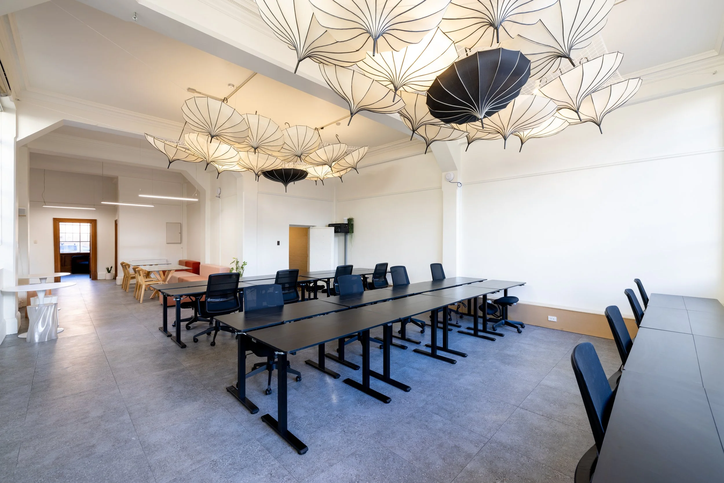 Empty modern conference room with black tables, black chairs, white walls, and umbrella-shaped ceiling lights.
