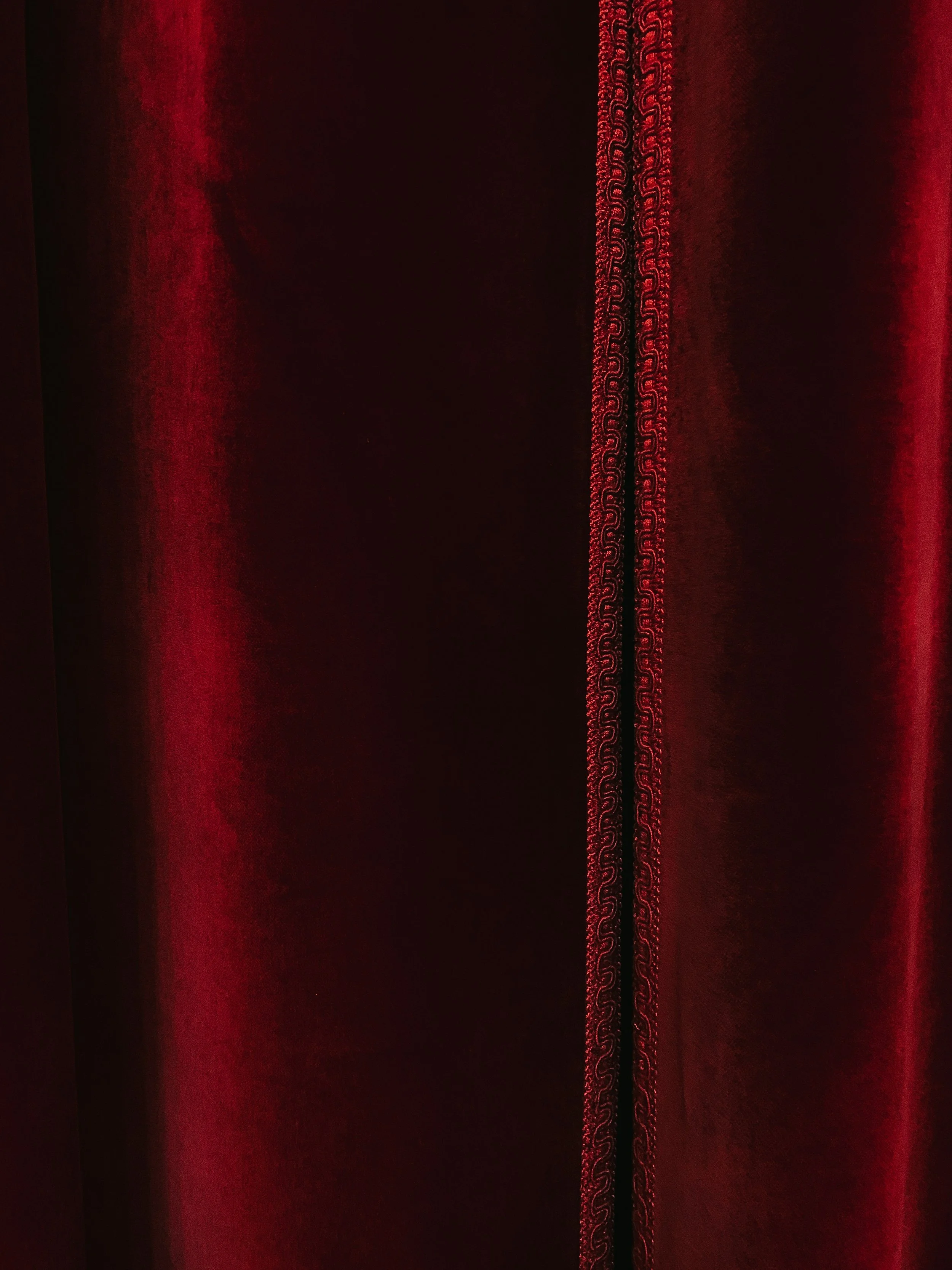 Close-up of a red velvet curtain with decorative trim.