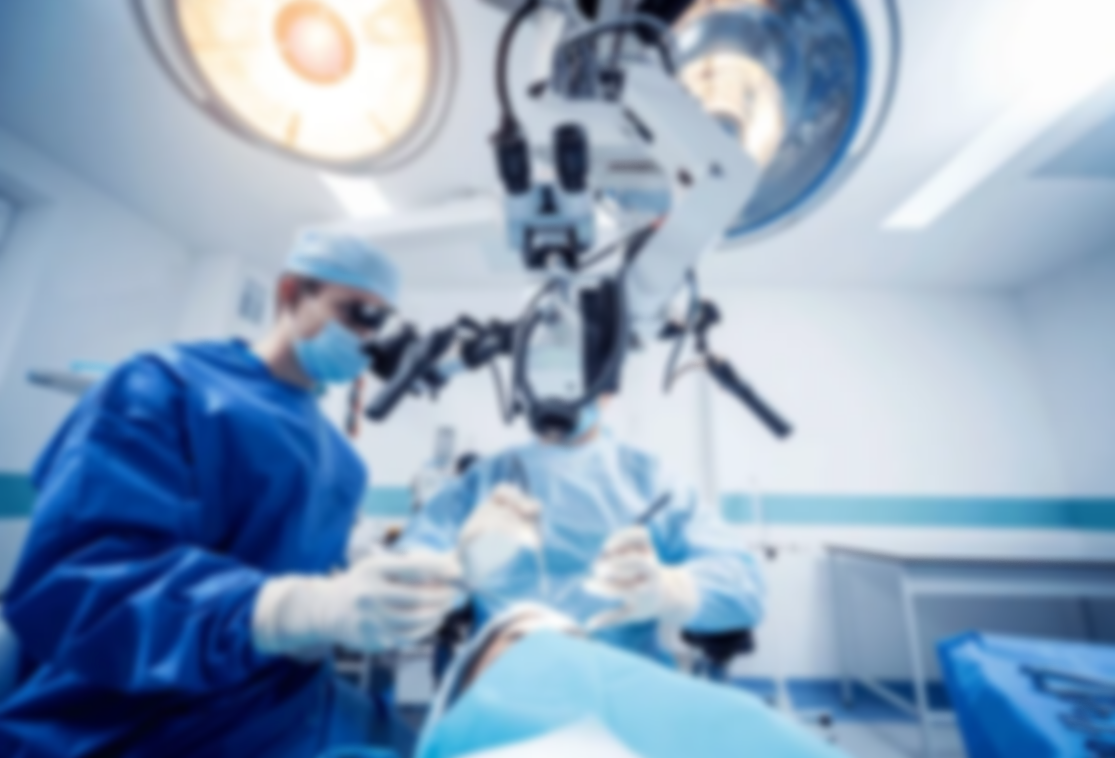 A medical team in blue scrubs and surgical masks performing an operation in a sterile operating room, viewed from beneath the surgical lights.