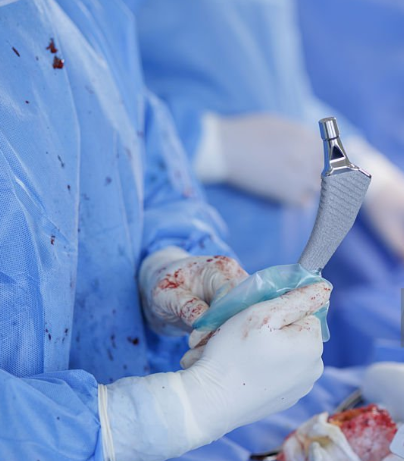 Surgeon in blue scrubs holding a surgical instrument in an operating room.