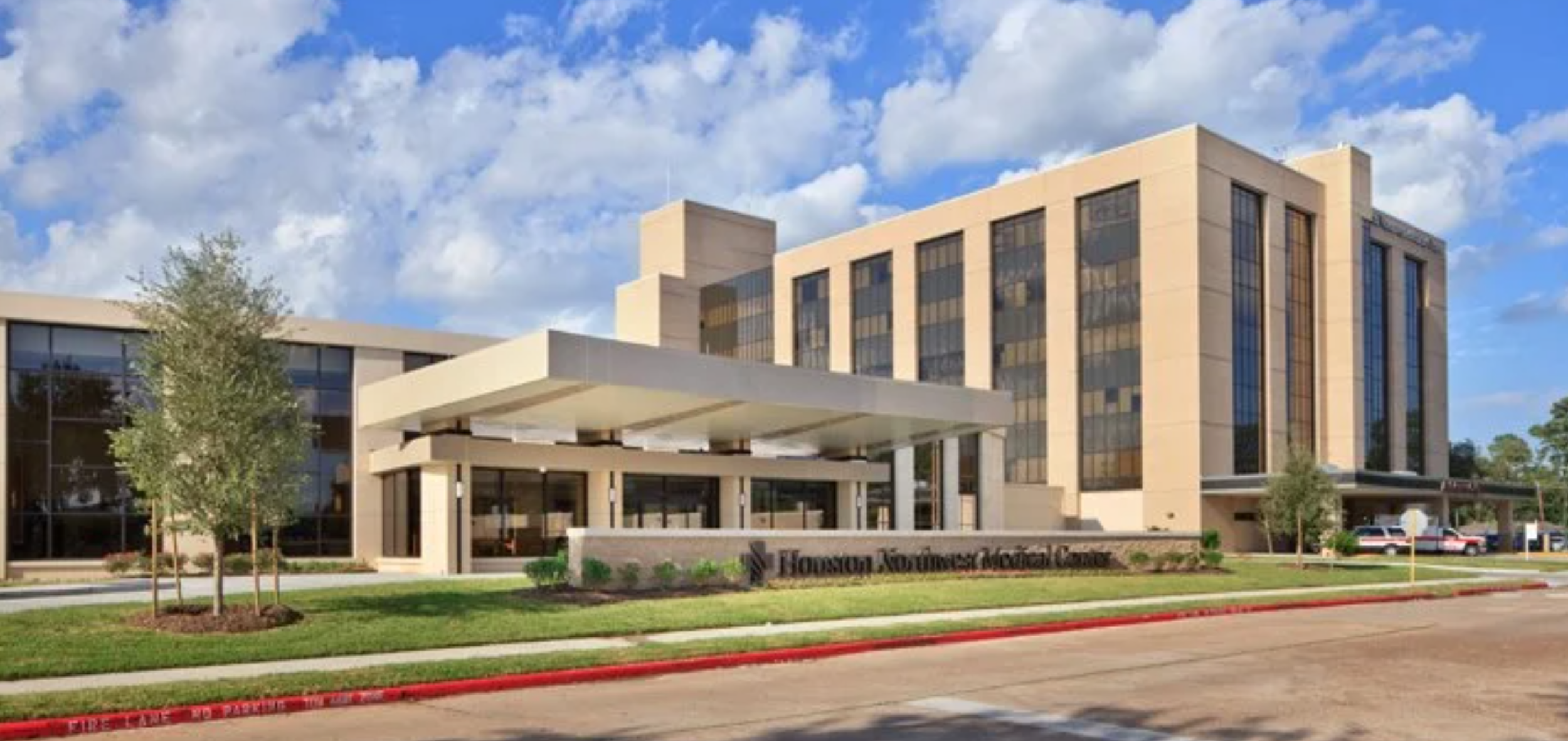 Exterior view of Houston Northwest Medical Center, a modern multi-story hospital building with large windows and a covered entrance, under a partly cloudy sky.