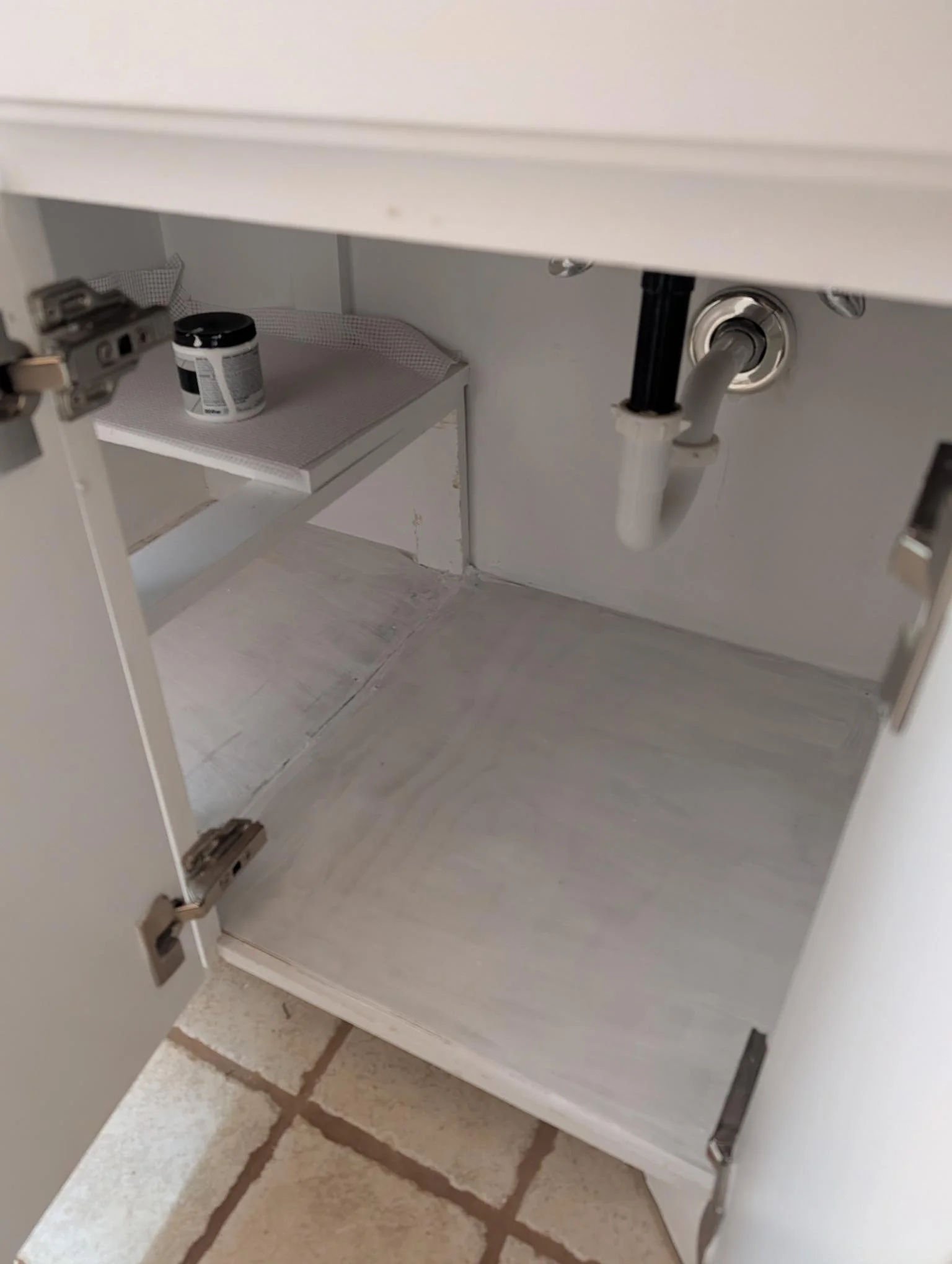 Open kitchen cabinet with plumbing pipes visible underneath.