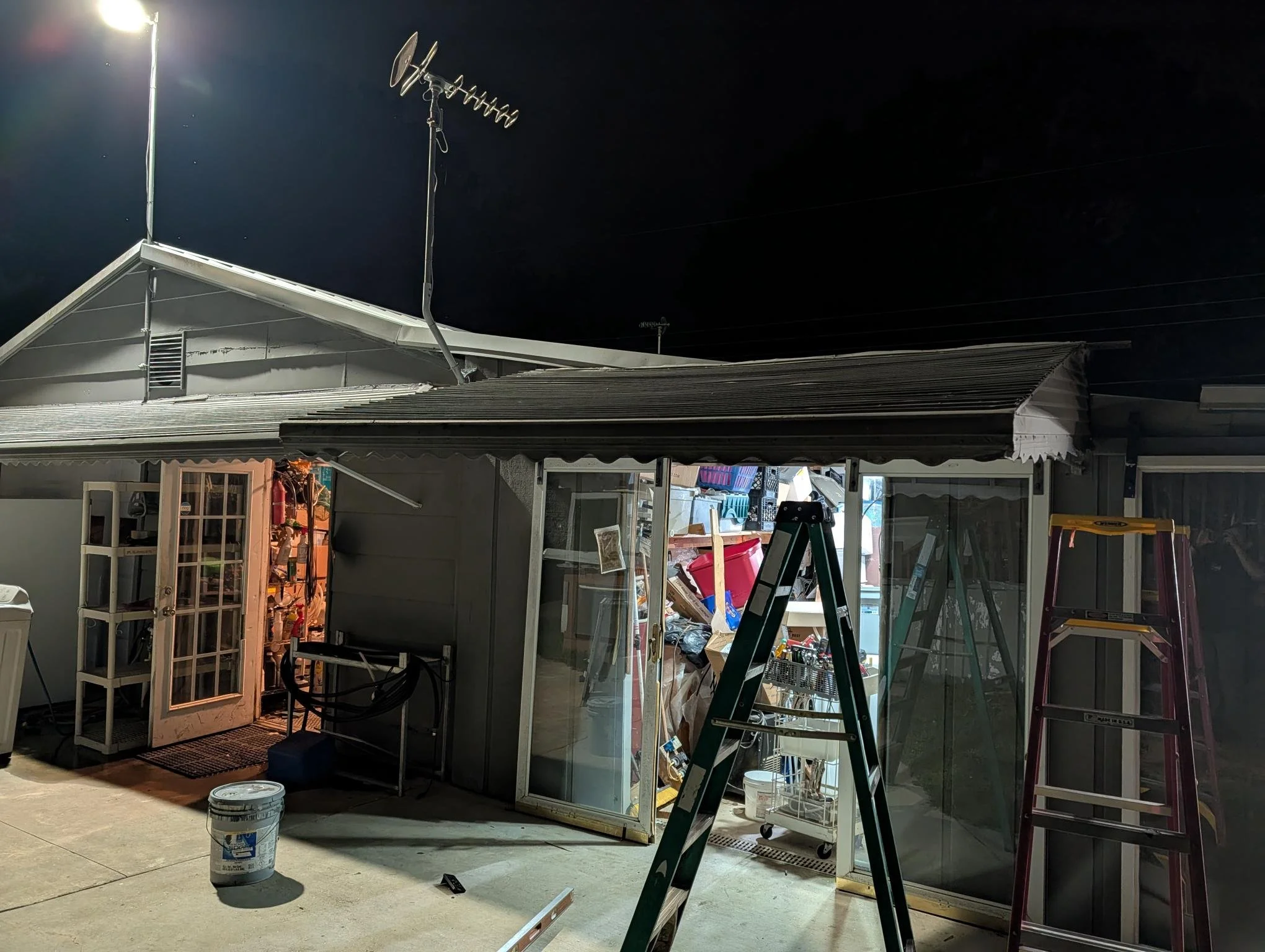 Backyard shed with ladders, tools, and supplies inside, illuminated at night.