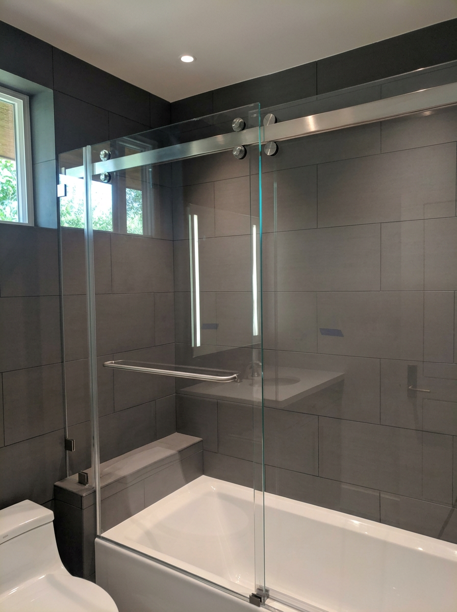 Bathroom with gray tiled walls, a glass shower enclosure, a small window, and a white toilet.