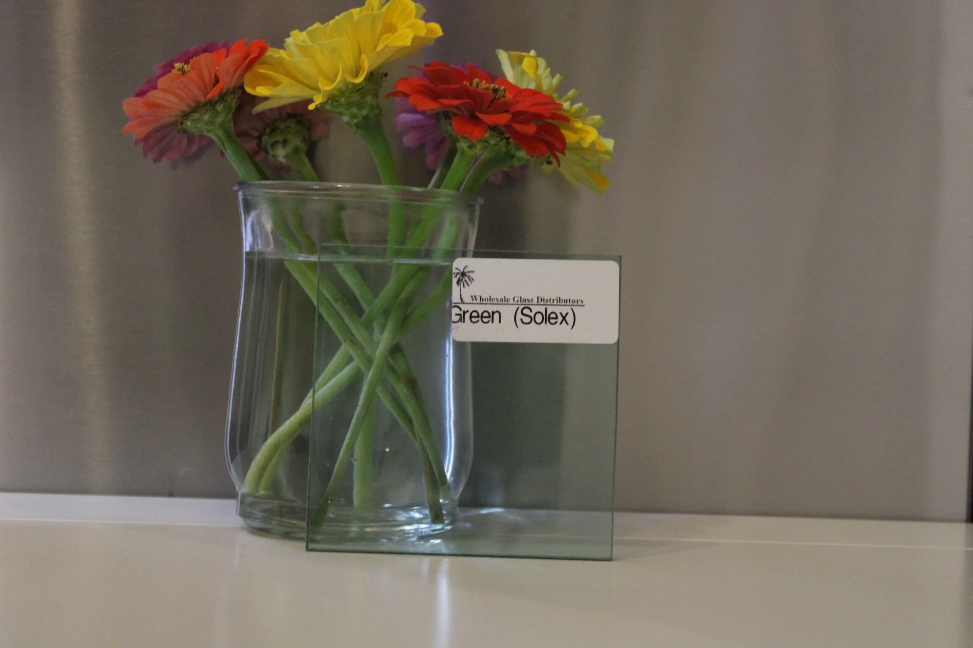 Colorful flowers in a glass vase with a label that reads "Wholesale Glass Distributors Green (Solex)."